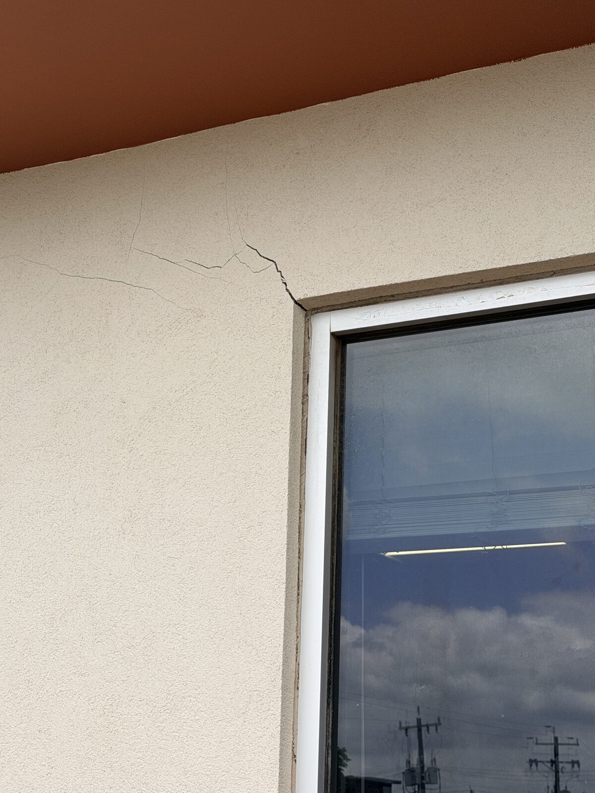 Diagonal crack radiating from a storefront window corner in stucco, a typical sign of commercial foundation settlement
