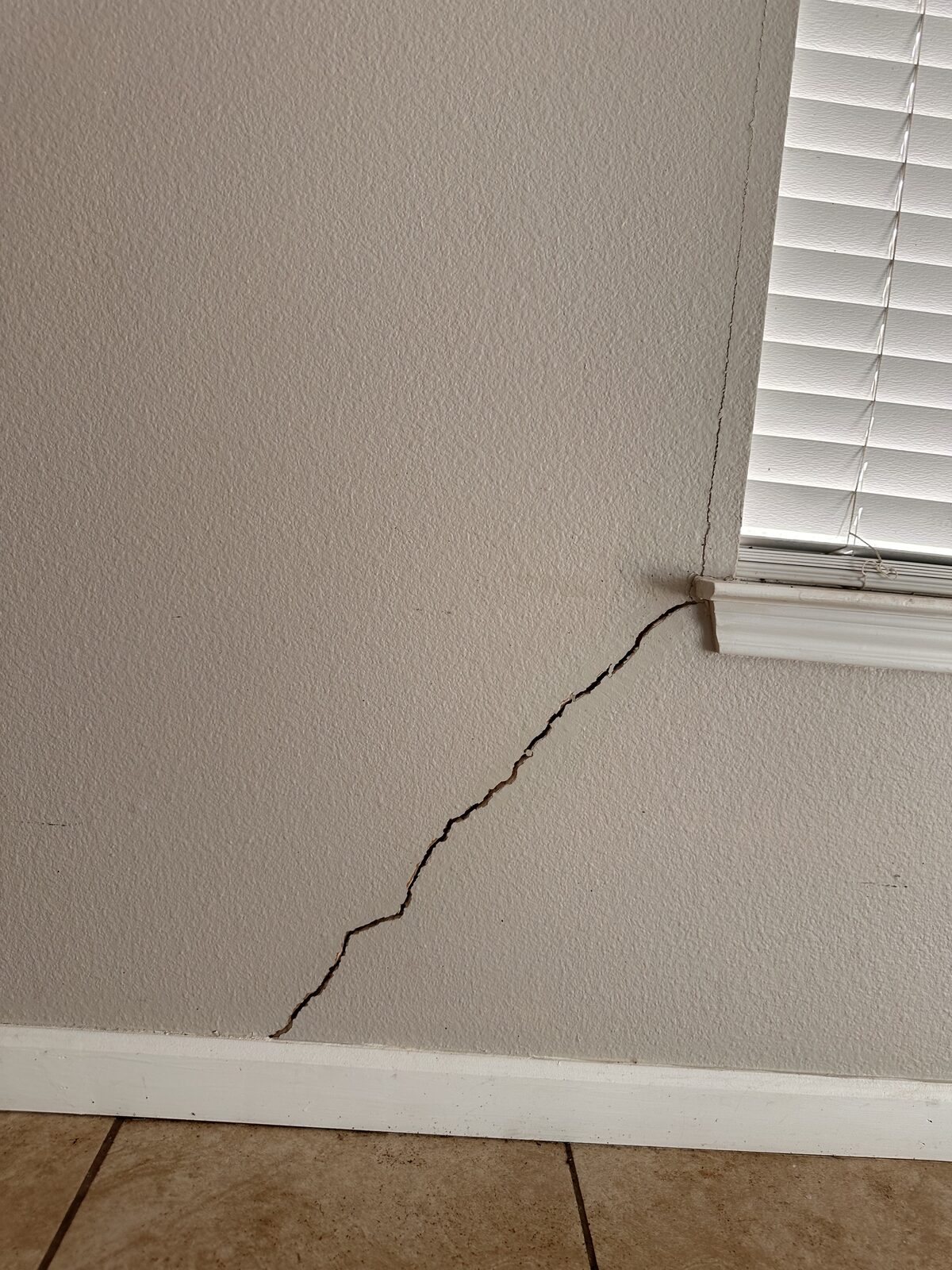 Diagonal drywall crack spreading from a window corner, a common interior sign of foundation movement