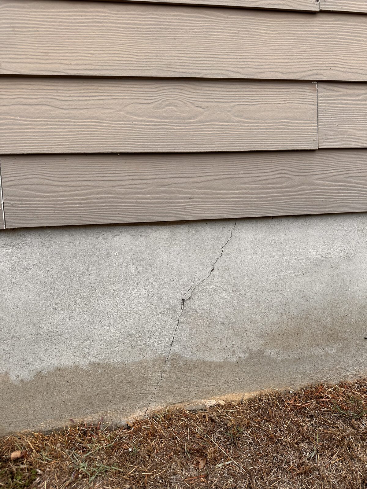 Diagonal crack in a concrete stem wall beneath lap siding, an exterior indicator of settlement
