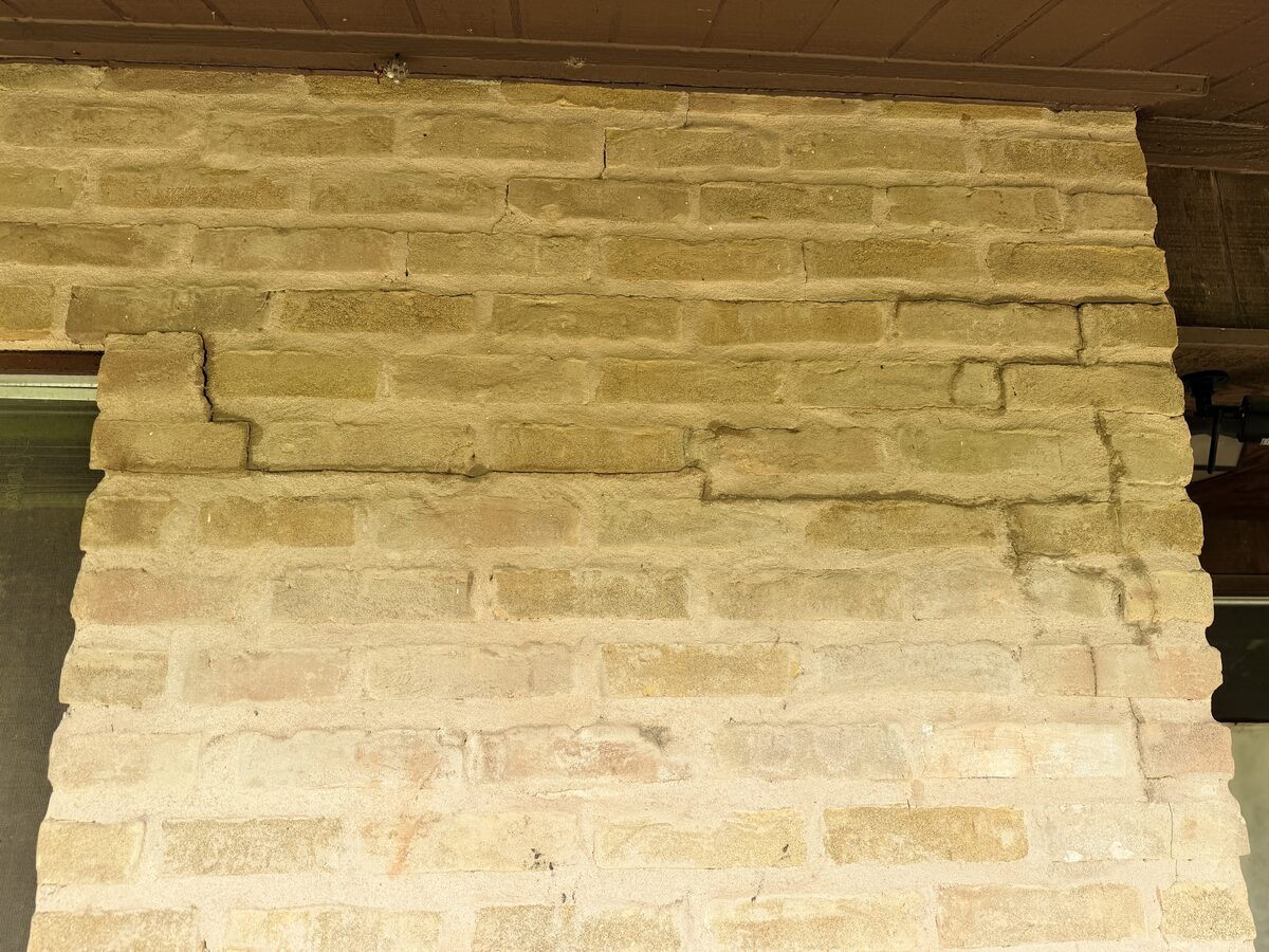 Close-up of displaced bricks and stepped cracking at a porch column, structural damage from foundation settlement