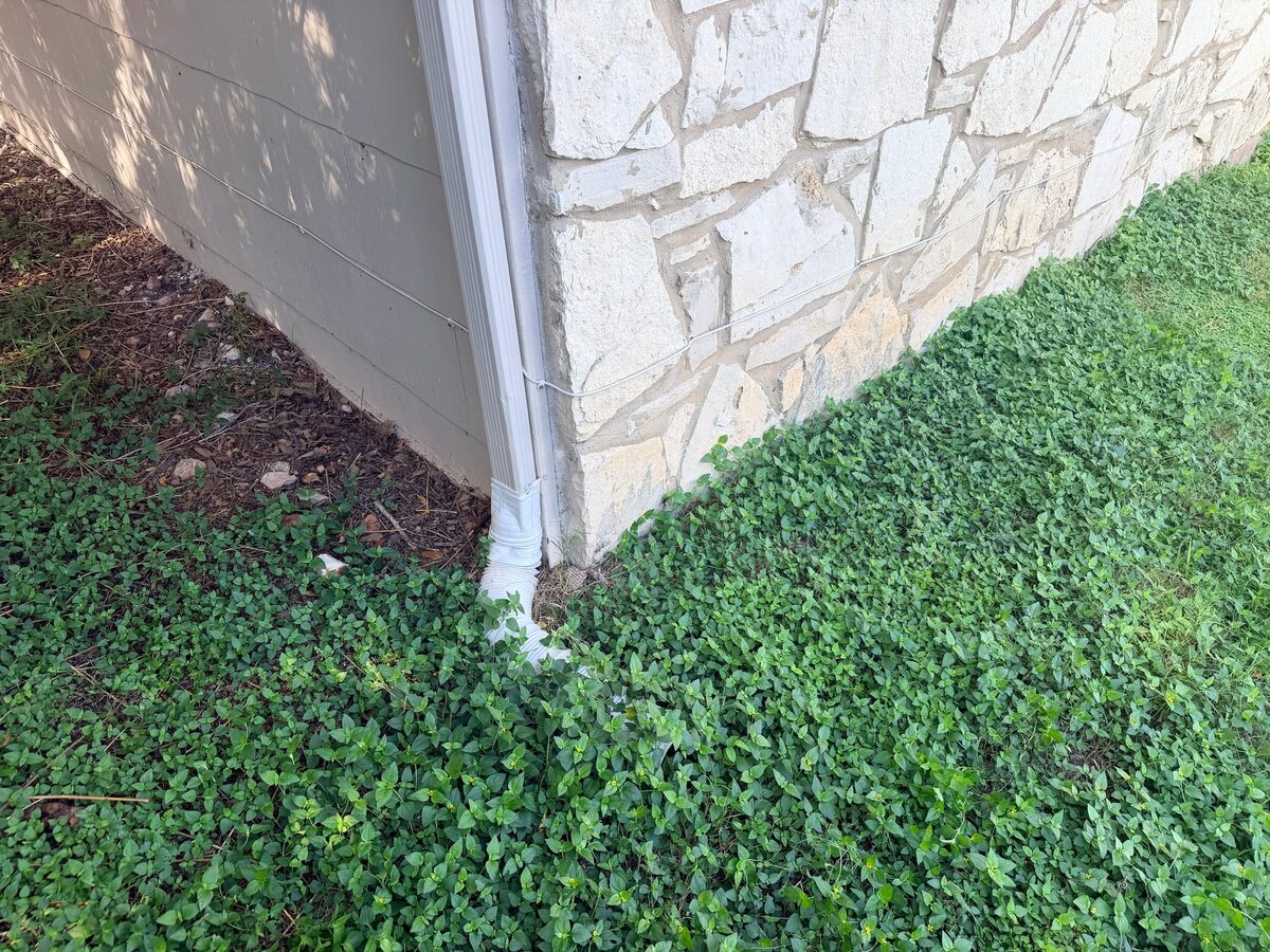 Downspout at the corner of a stone veneer house emptying straight into ground cover at the slab
