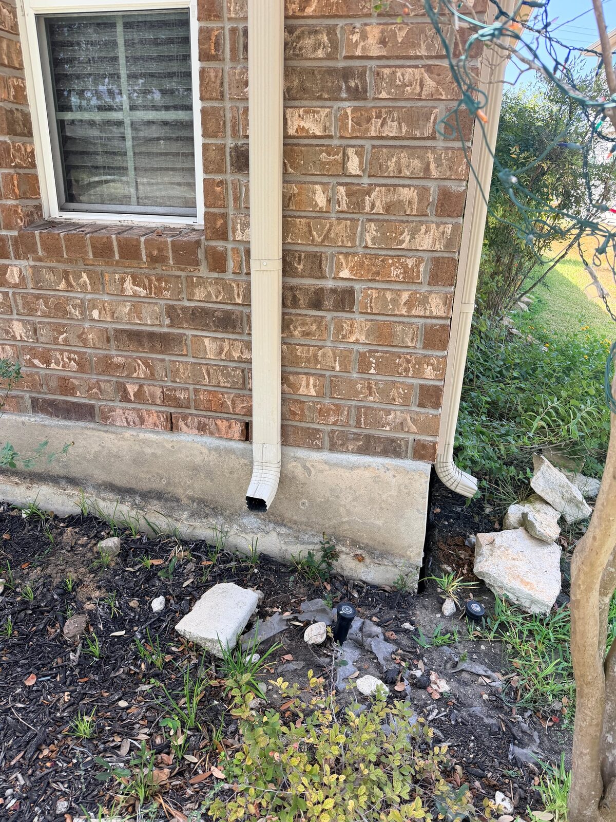Two downspouts dumping at a brick house foundation with broken splash blocks
