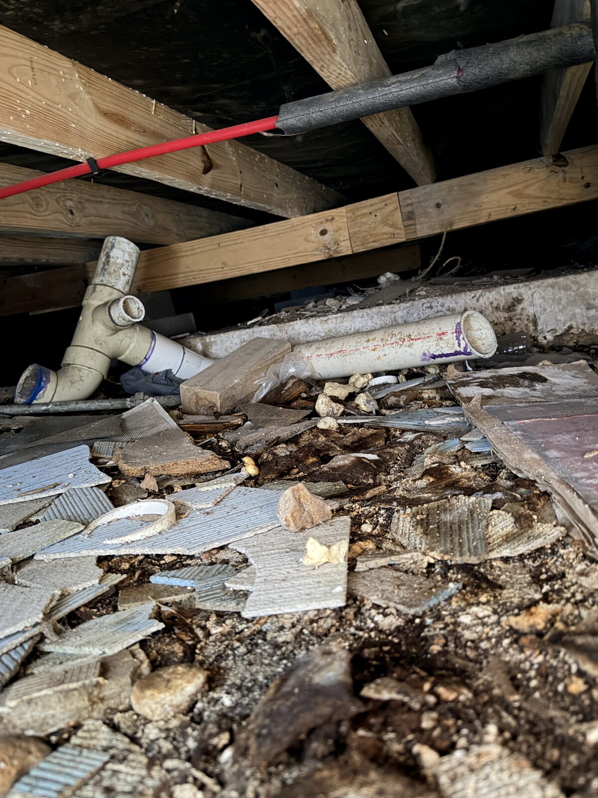 PVC drain lines beside a debris filled soil bank under a house