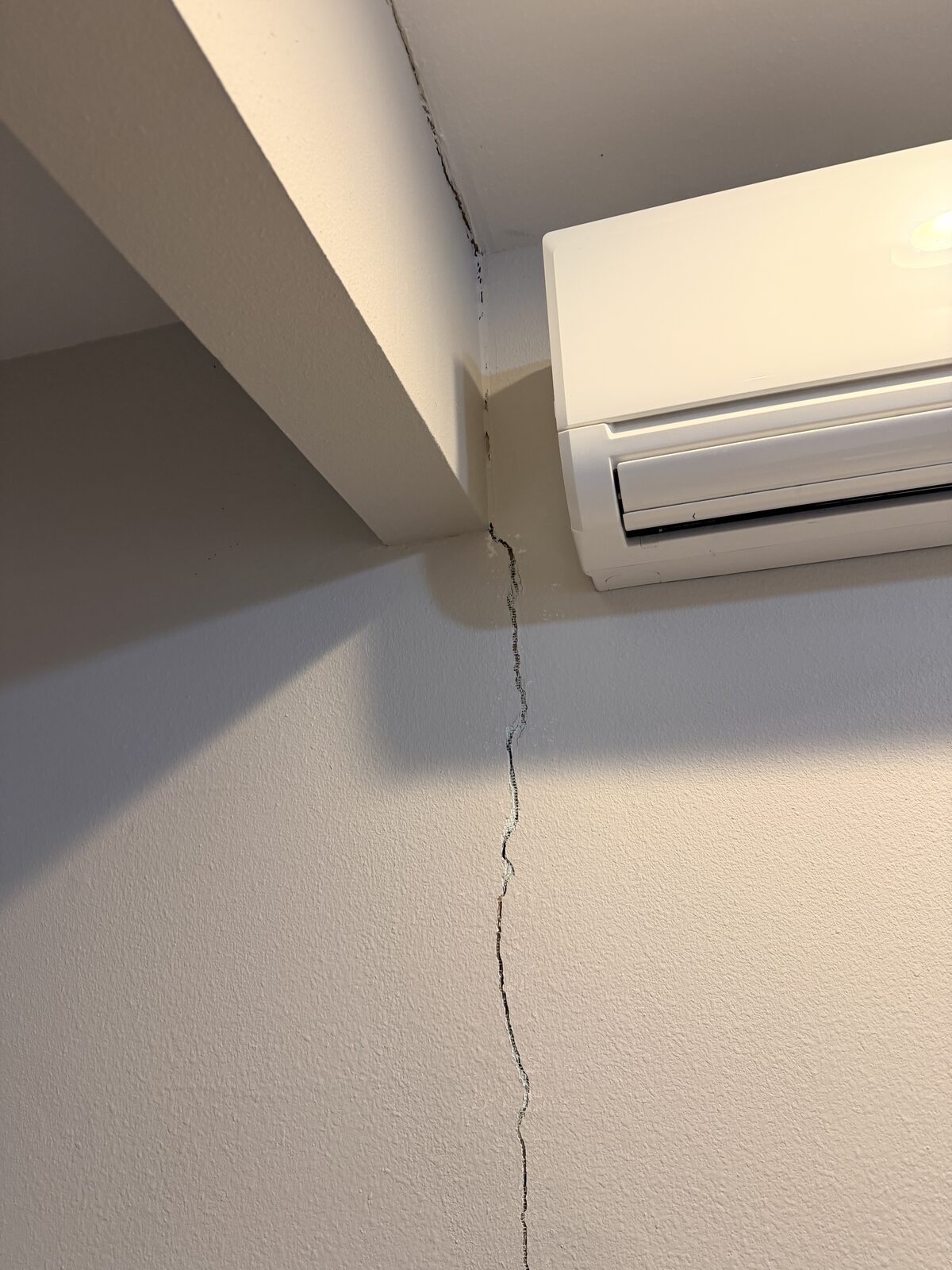 Drywall crack dropping from a ceiling beam corner, an interior sign of foundation settlement
