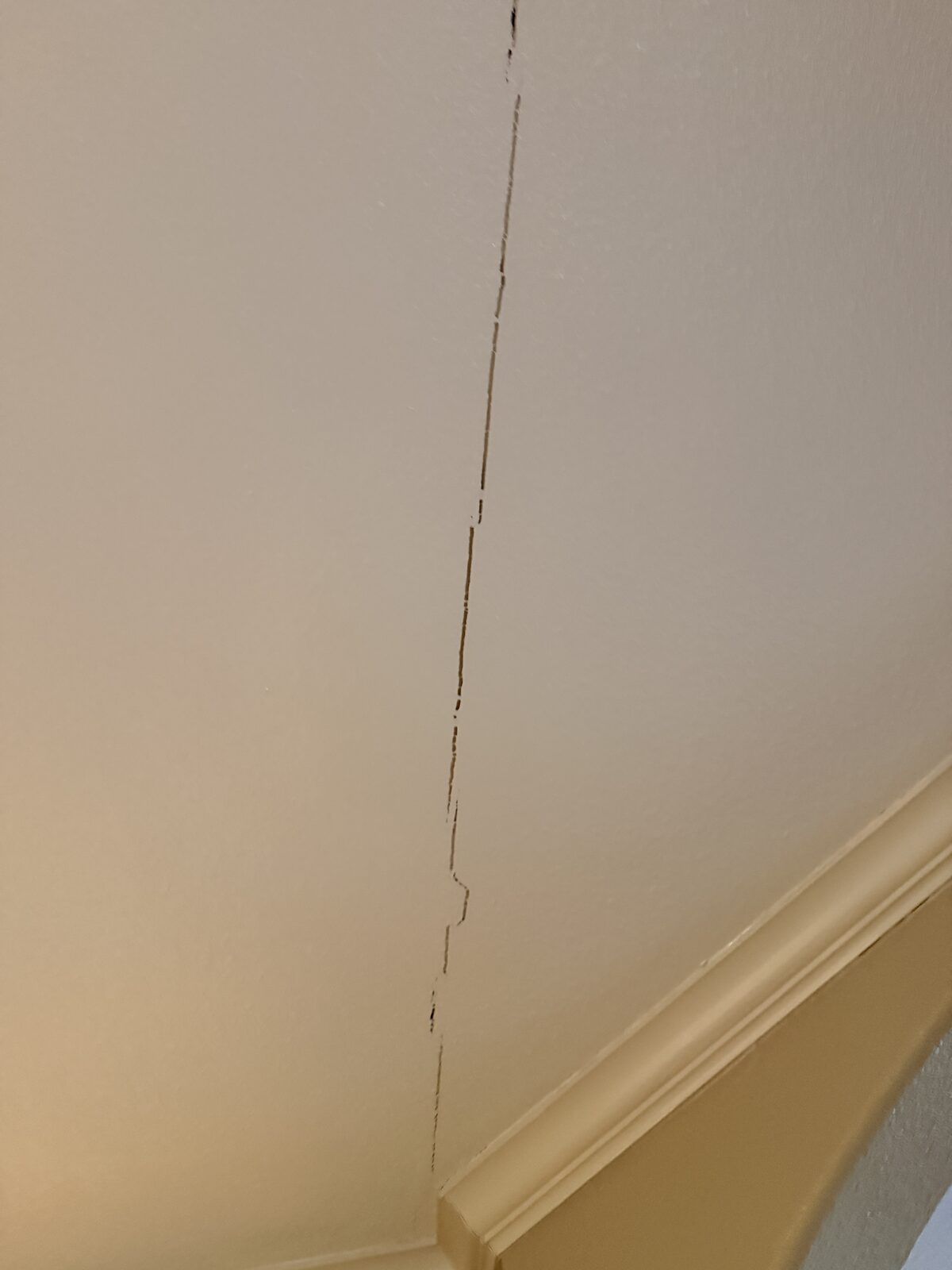 Hairline drywall crack running down an interior wall from the crown molding, often caused by foundation movement