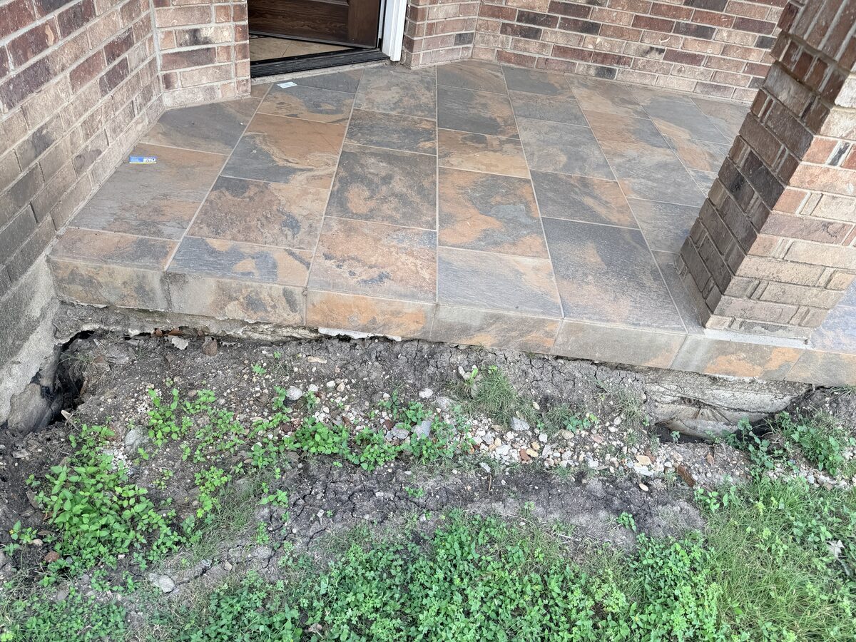 Erosion along a flagstone patio edge exposing the slab foundation beneath a brick wall