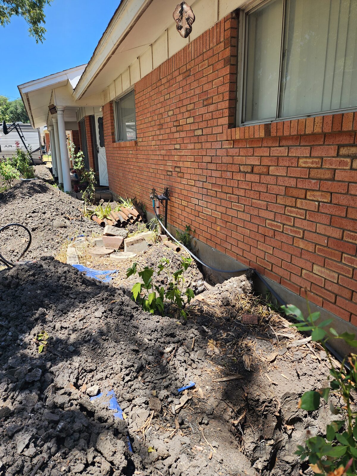 Soil excavated and piled along a brick home's foundation during underpinning pier installation