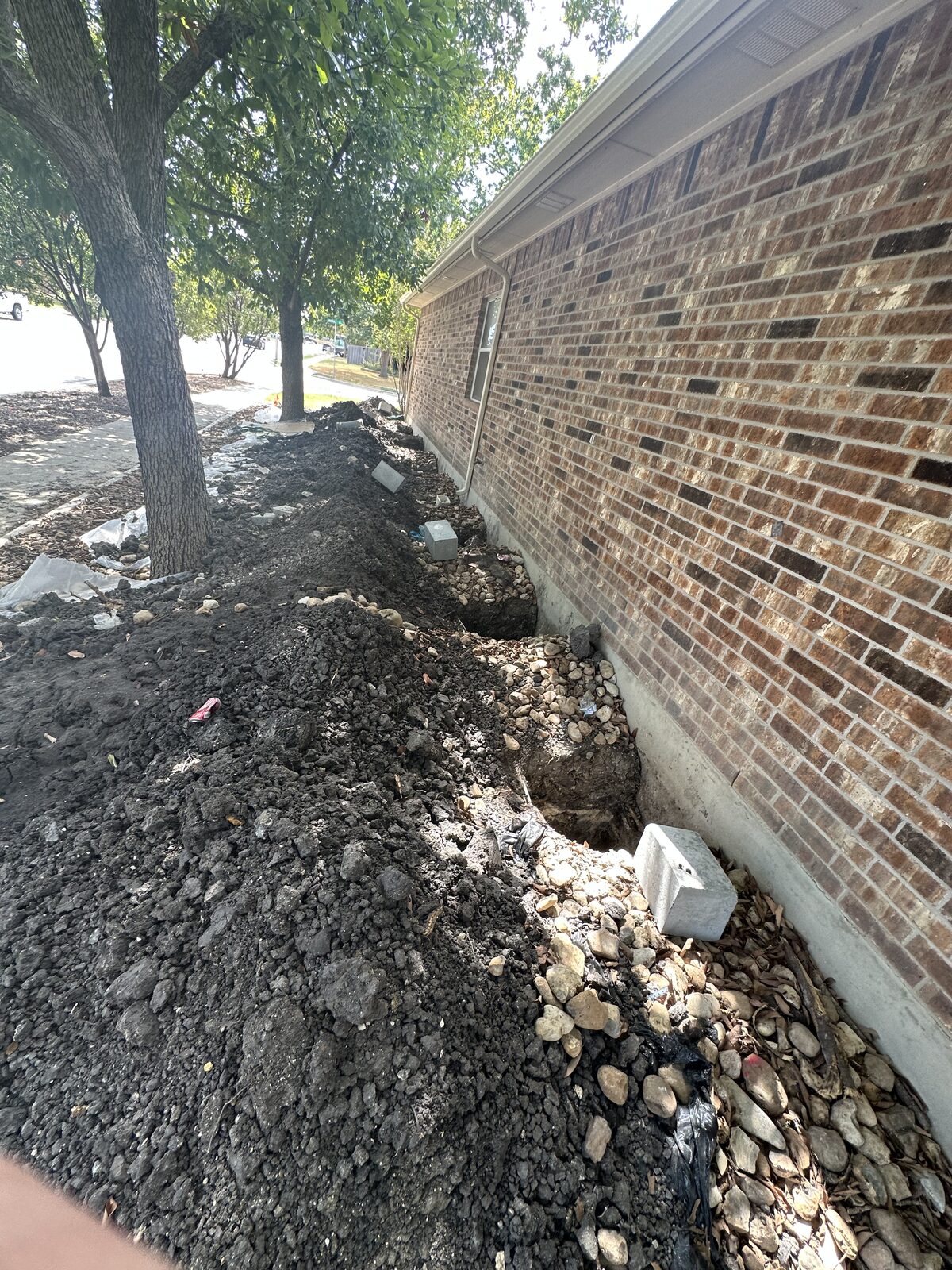 Excavation line with spoil and open pier pits along the brick wall of a home during foundation repair
