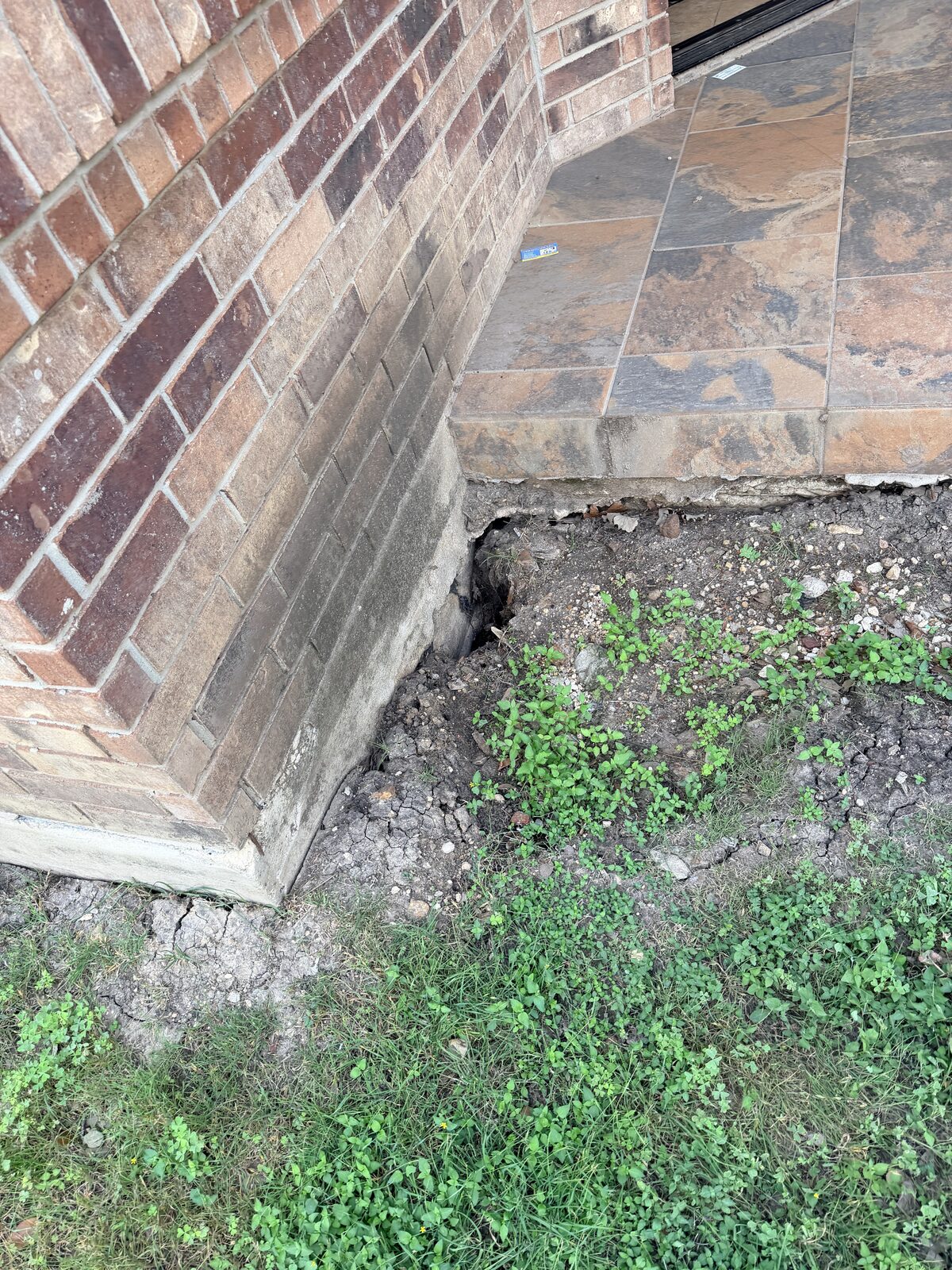 Exposed concrete foundation corner with a soil gap beneath the brick veneer of a Central Texas home