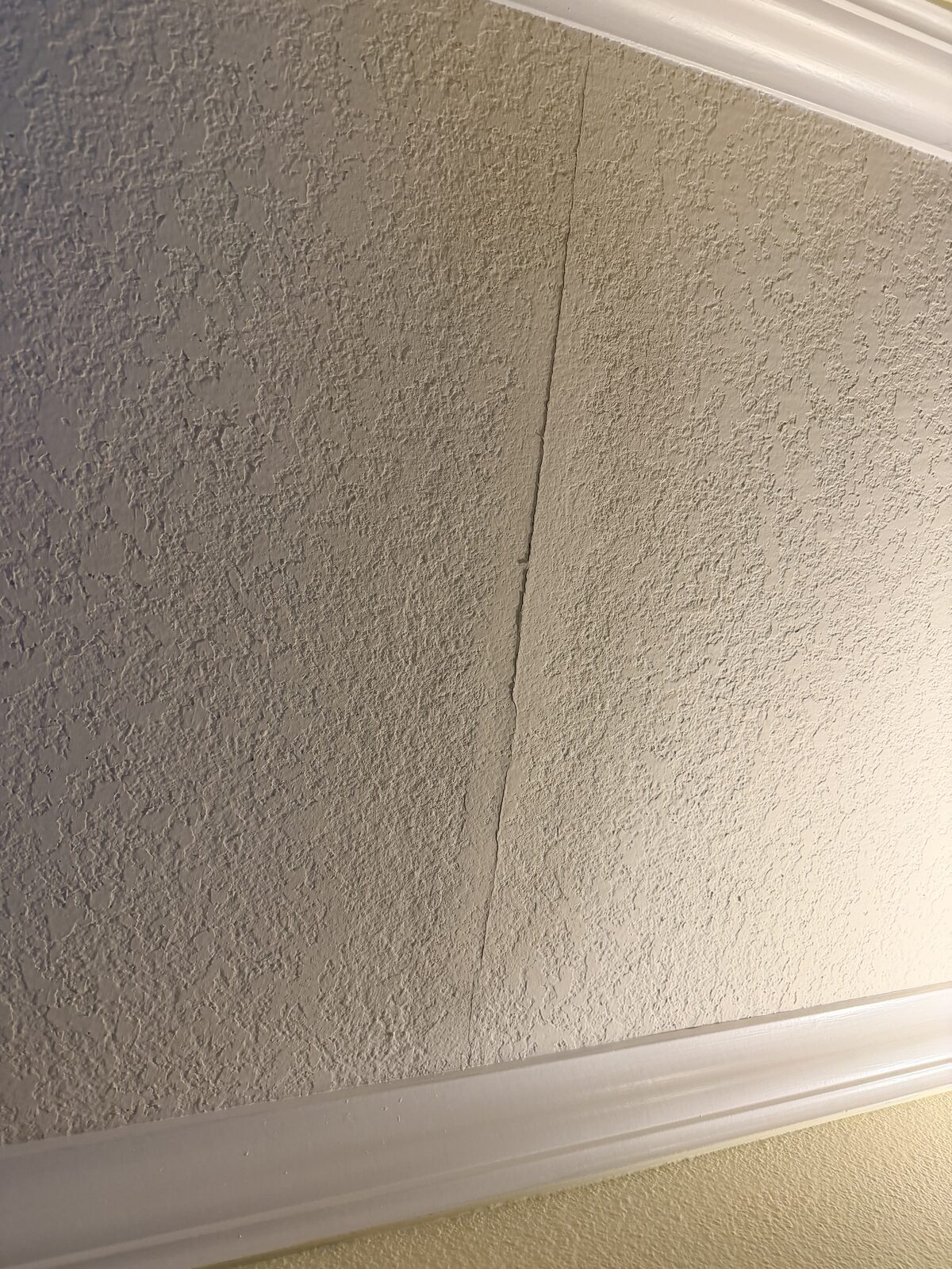 Faint vertical crack running down a heavily textured knockdown wall between crown molding runs