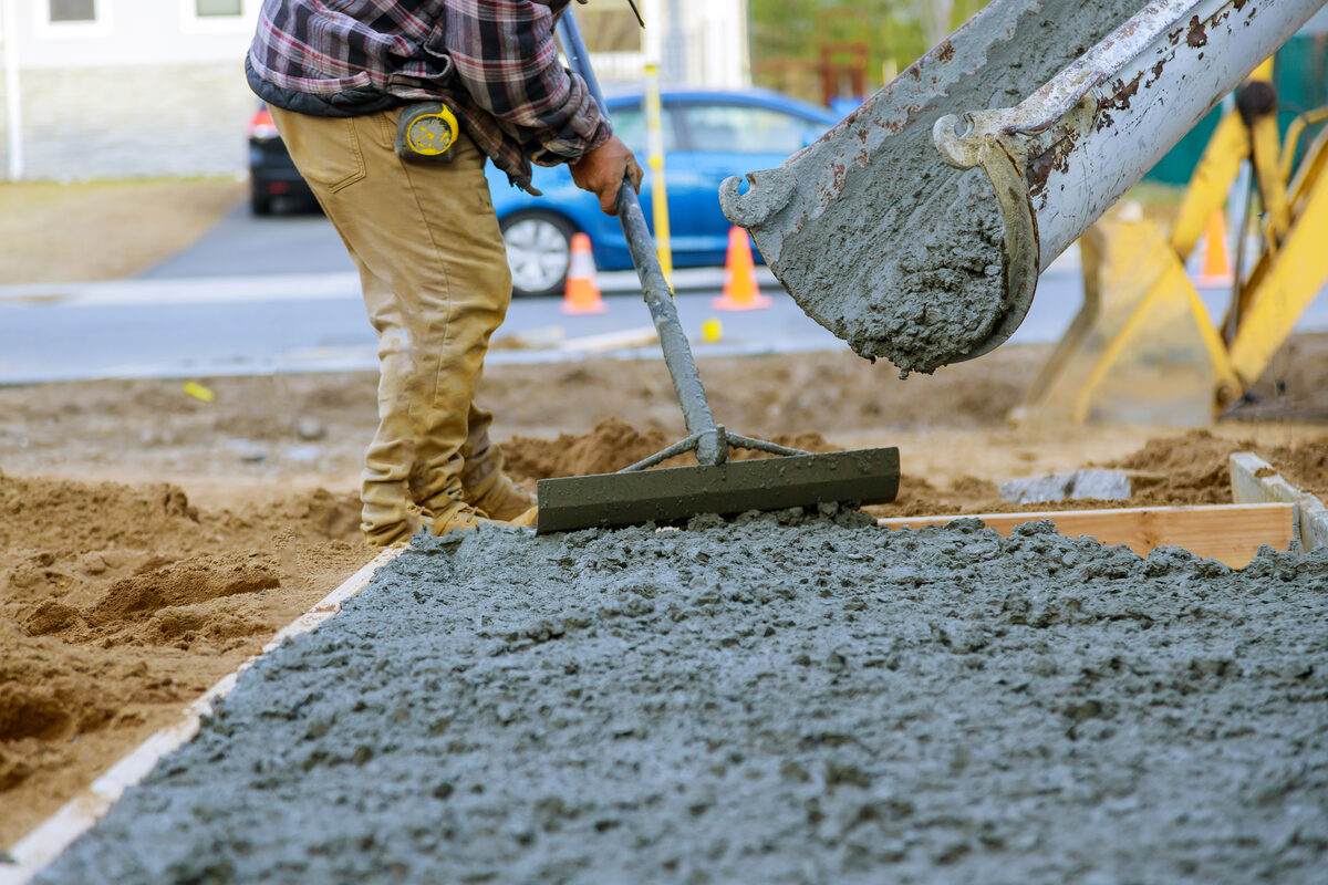 Worker spreading wet concrete from a truck chute into wooden forms on pour day