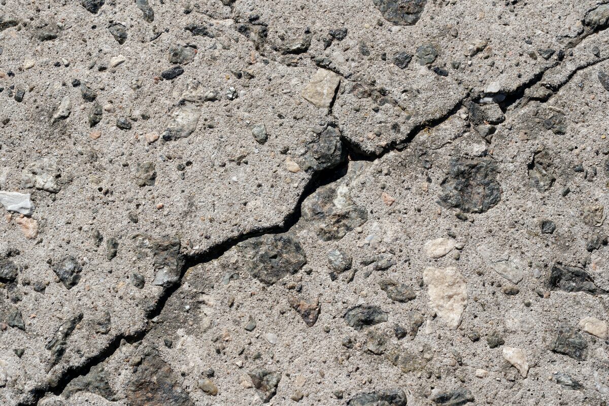 Close-up of a large crack running through old, unreinforced concrete with exposed aggregate