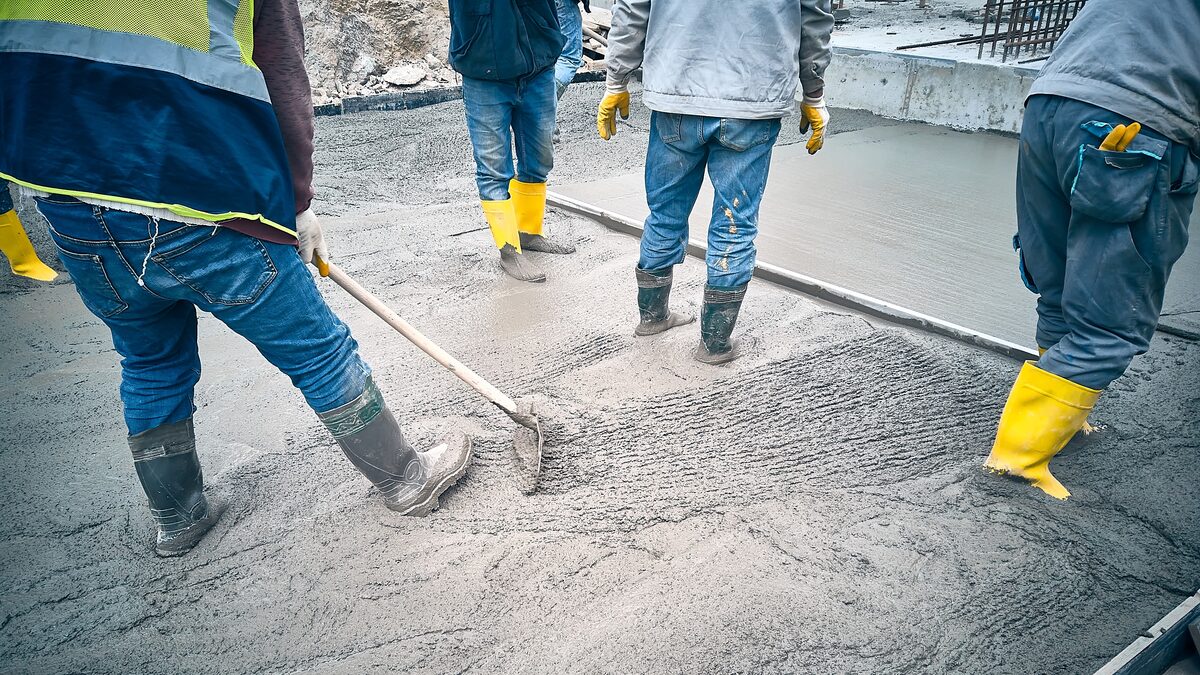 Concrete crew raking and spreading a fresh pour to an even depth across a slab