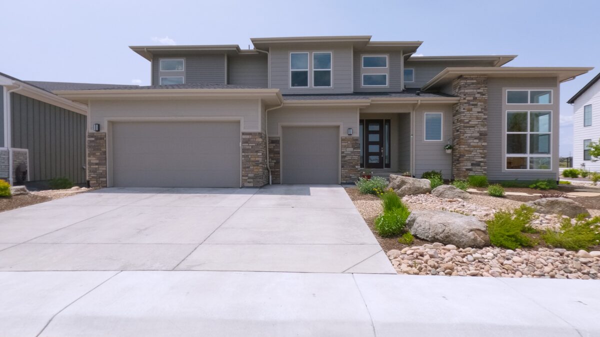 Finished broom-finish concrete driveway leading to a modern two-story home with a three-car garage