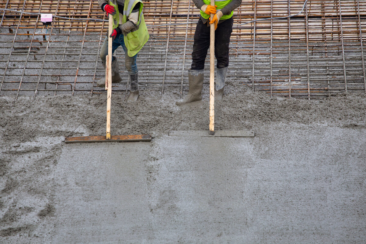 Two workers screeding a large concrete slab poured over a steel rebar reinforcement mat
