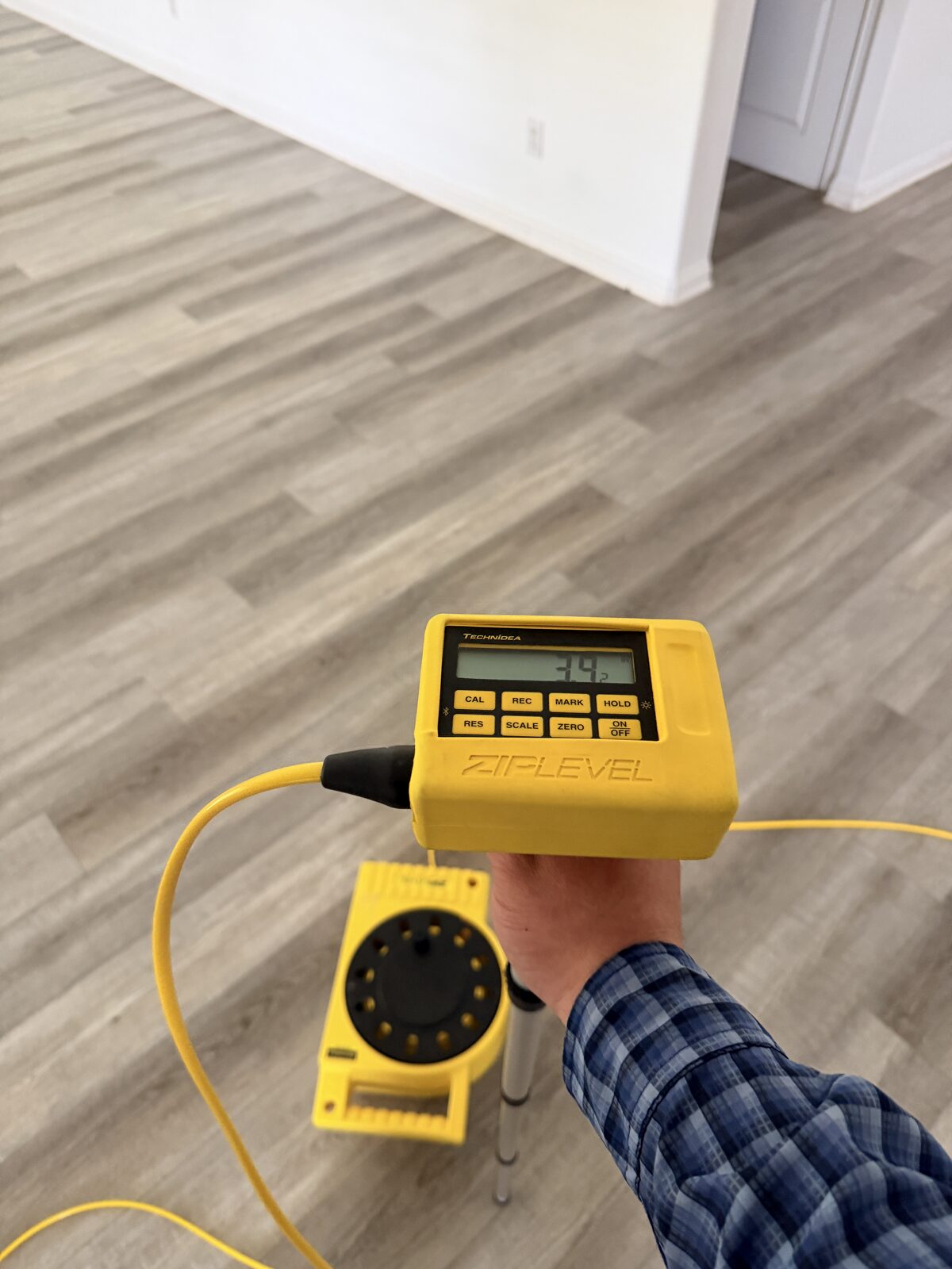 Hand holding a ZipLevel elevation meter over vinyl plank flooring during a floor survey