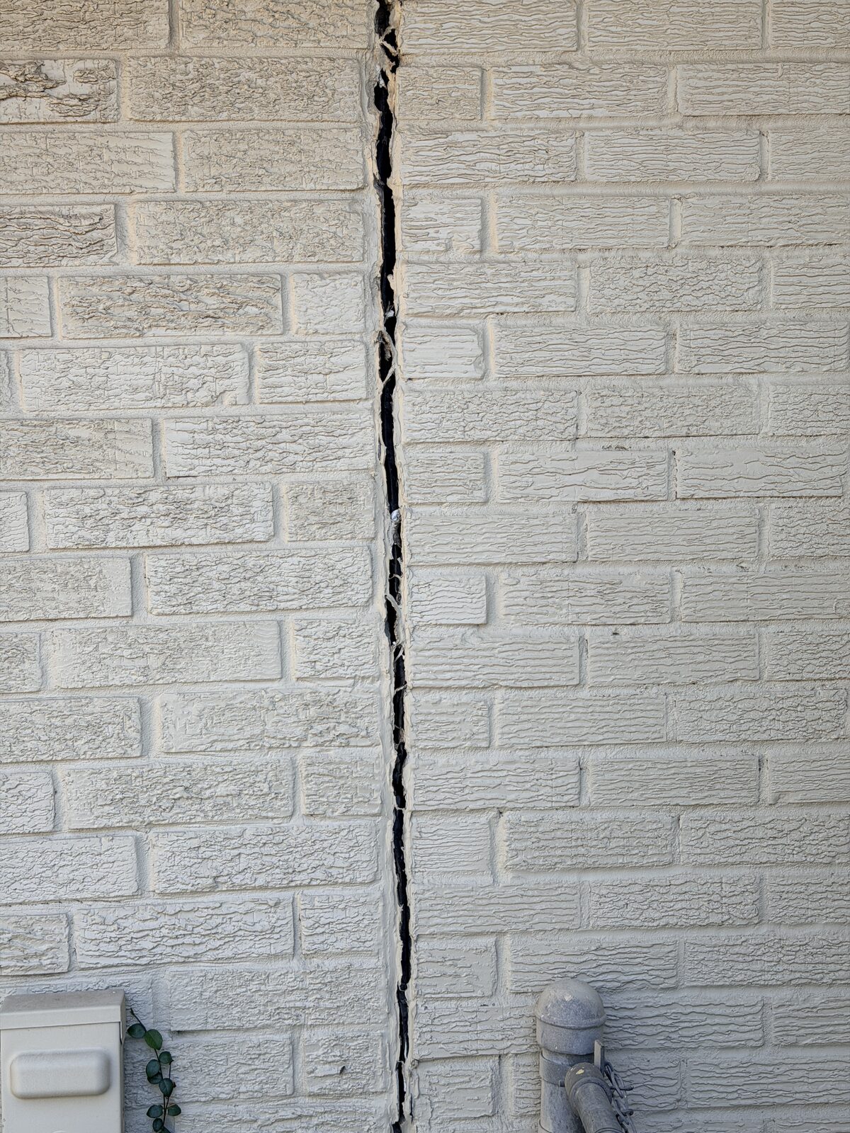 Full-height crack running through a painted brick wall