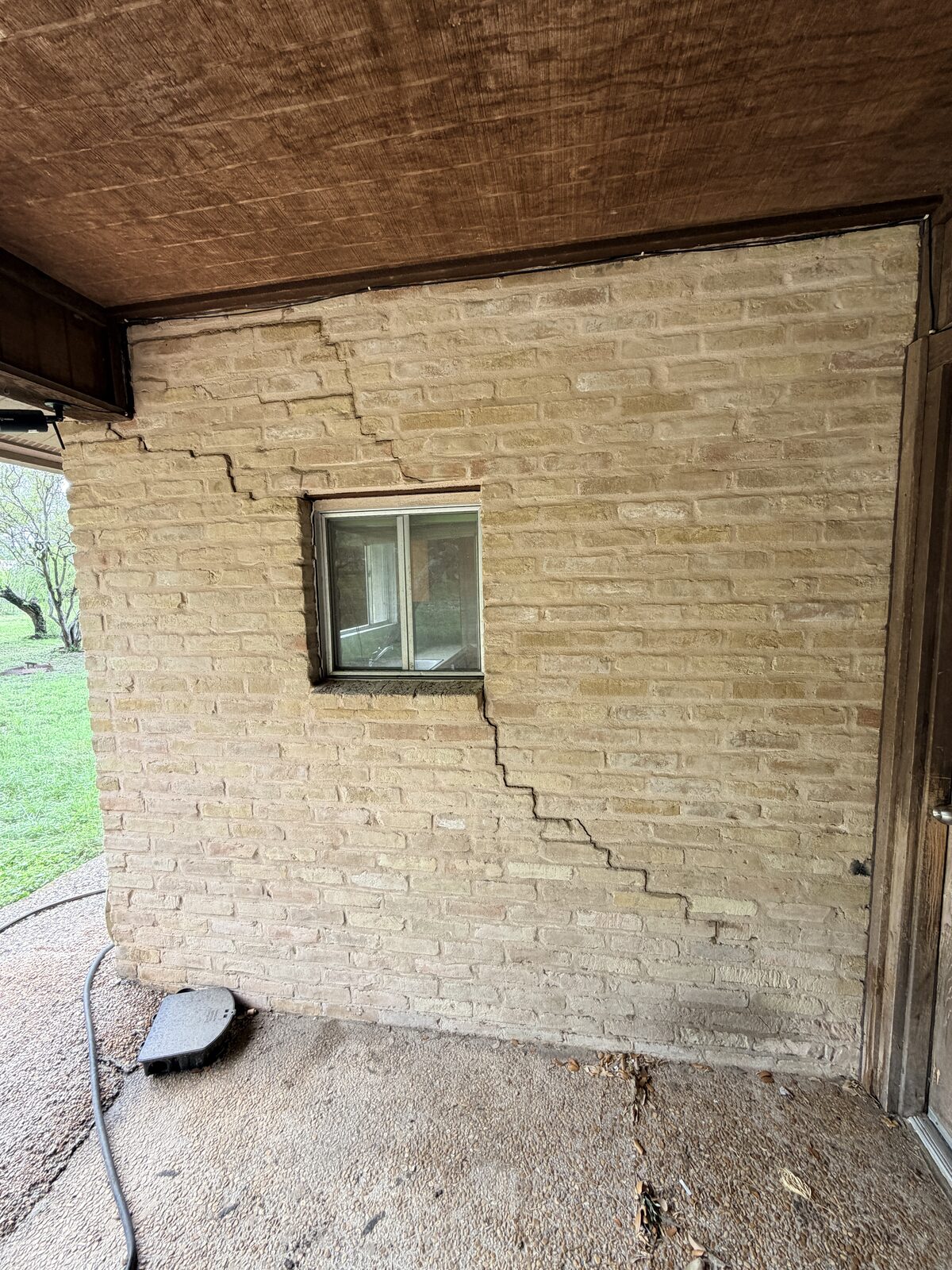 Severe stair-step crack running the full height of a tan brick porch wall, classic foundation settlement damage