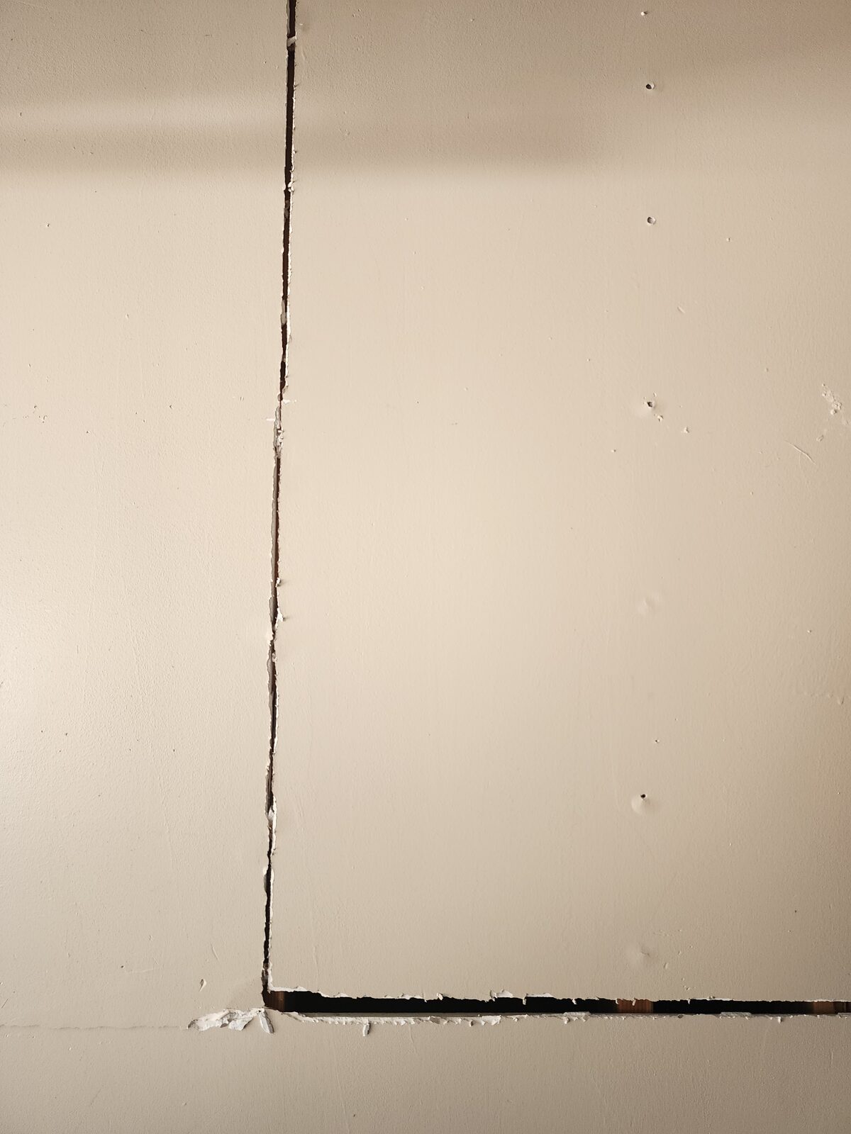 Vertical and horizontal cracks along drywall seams inside a garage, an interior sign of foundation settlement