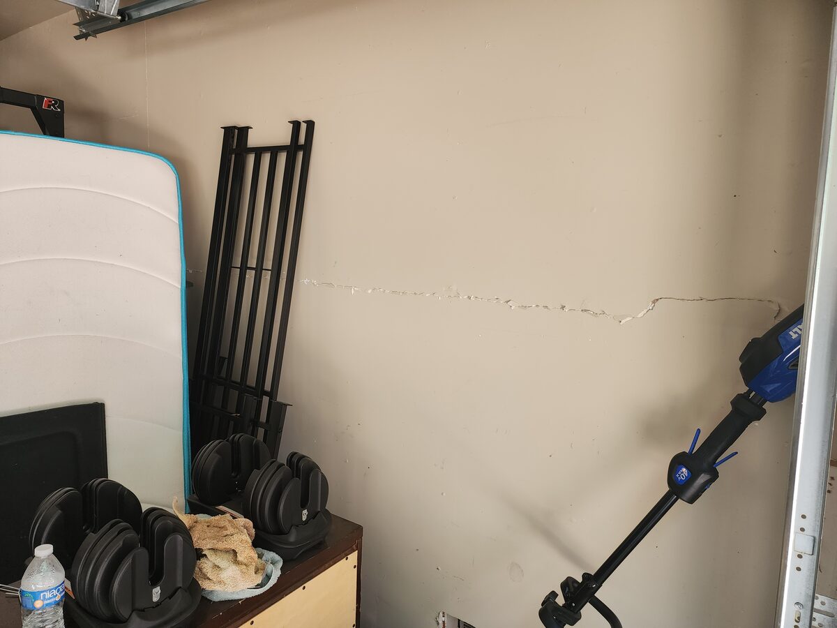 Horizontal settlement crack across a garage wall behind stored equipment, noted during a foundation repair inspection