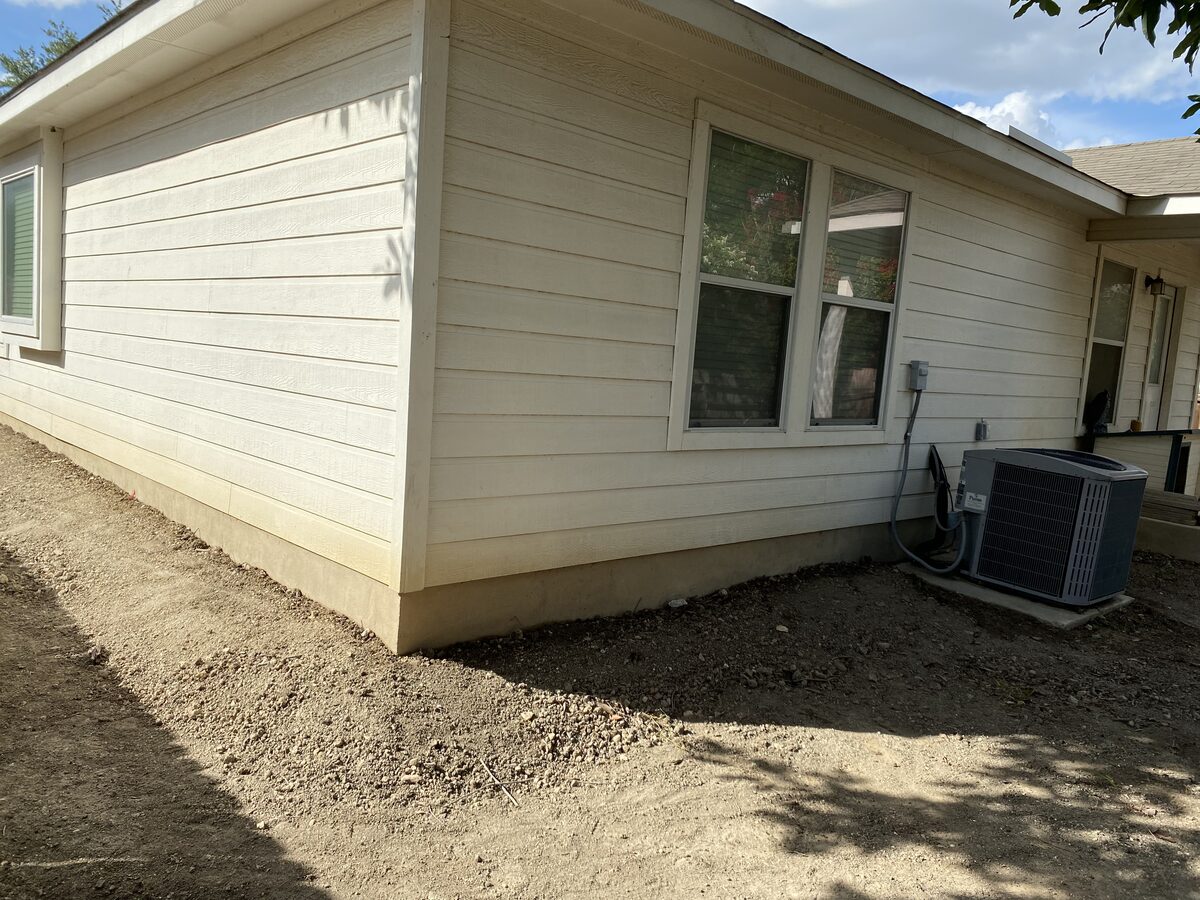 Freshly graded soil around a home's slab foundation after pier installation and backfill