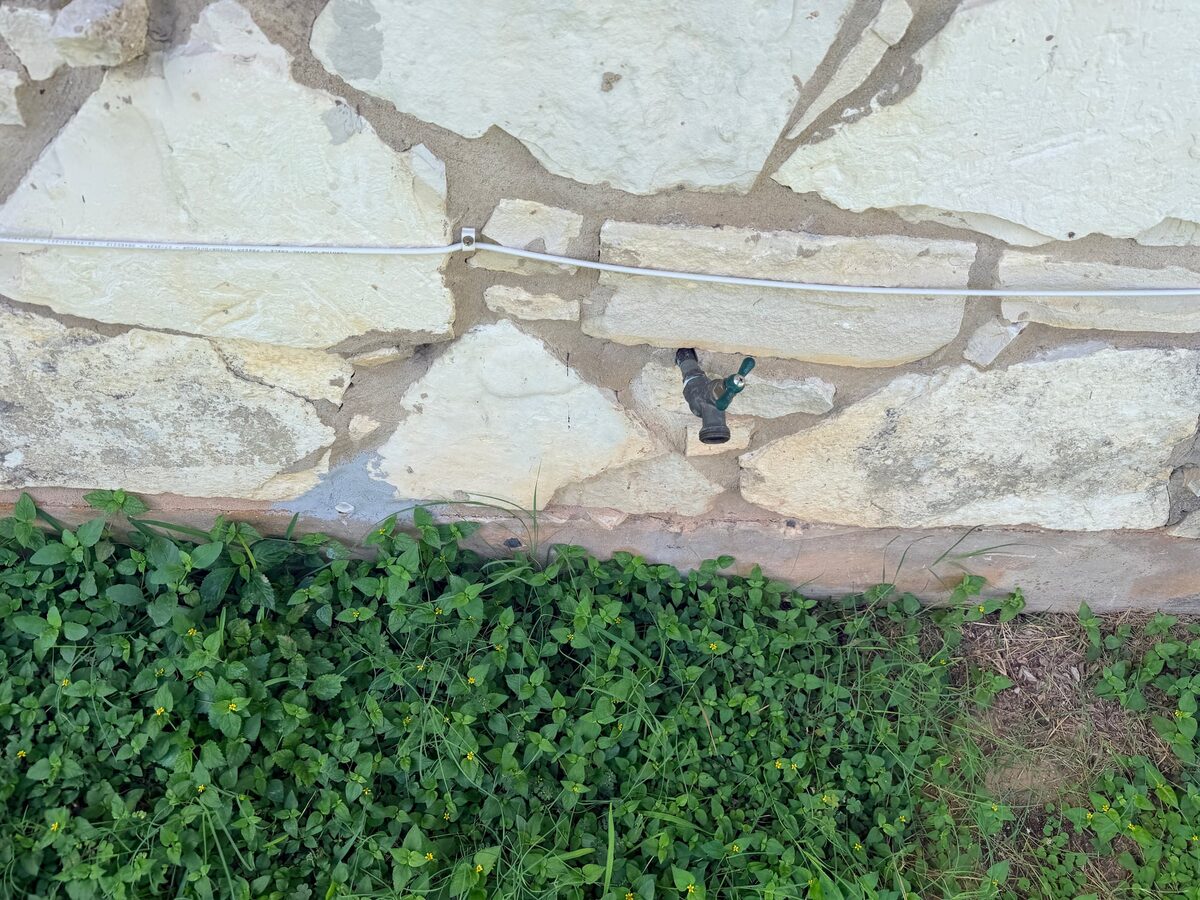 Stone veneer wall with a hose bib and thick ground cover planted right up to the slab edge