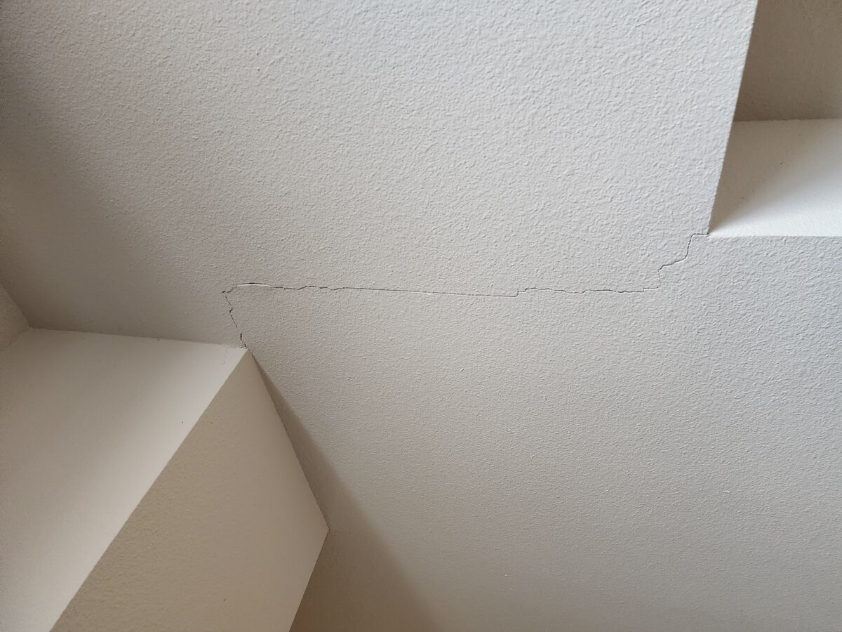 Hairline crack running across a textured ceiling above a stairwell, an interior indicator of foundation movement
