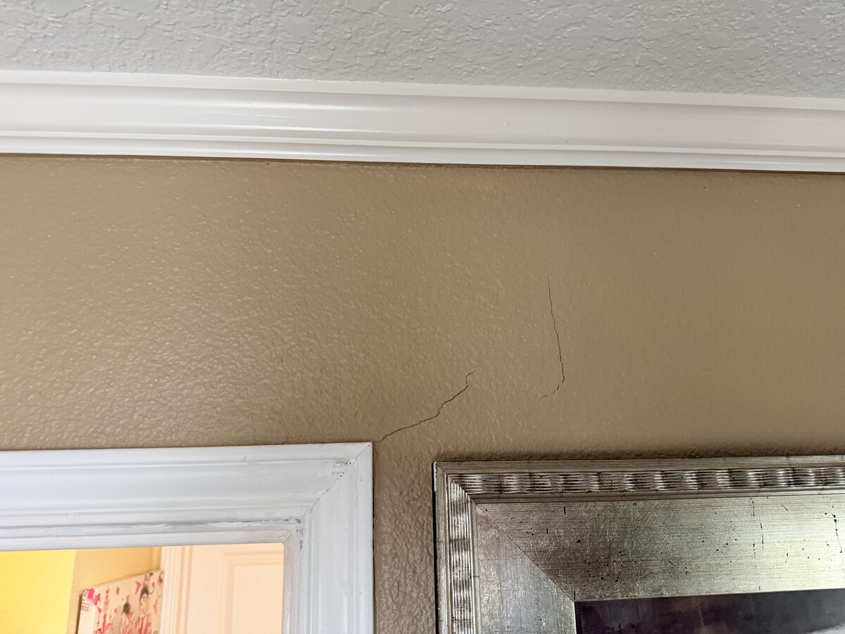 Hairline crack descending from crown molding in a hallway, noted during foundation inspection