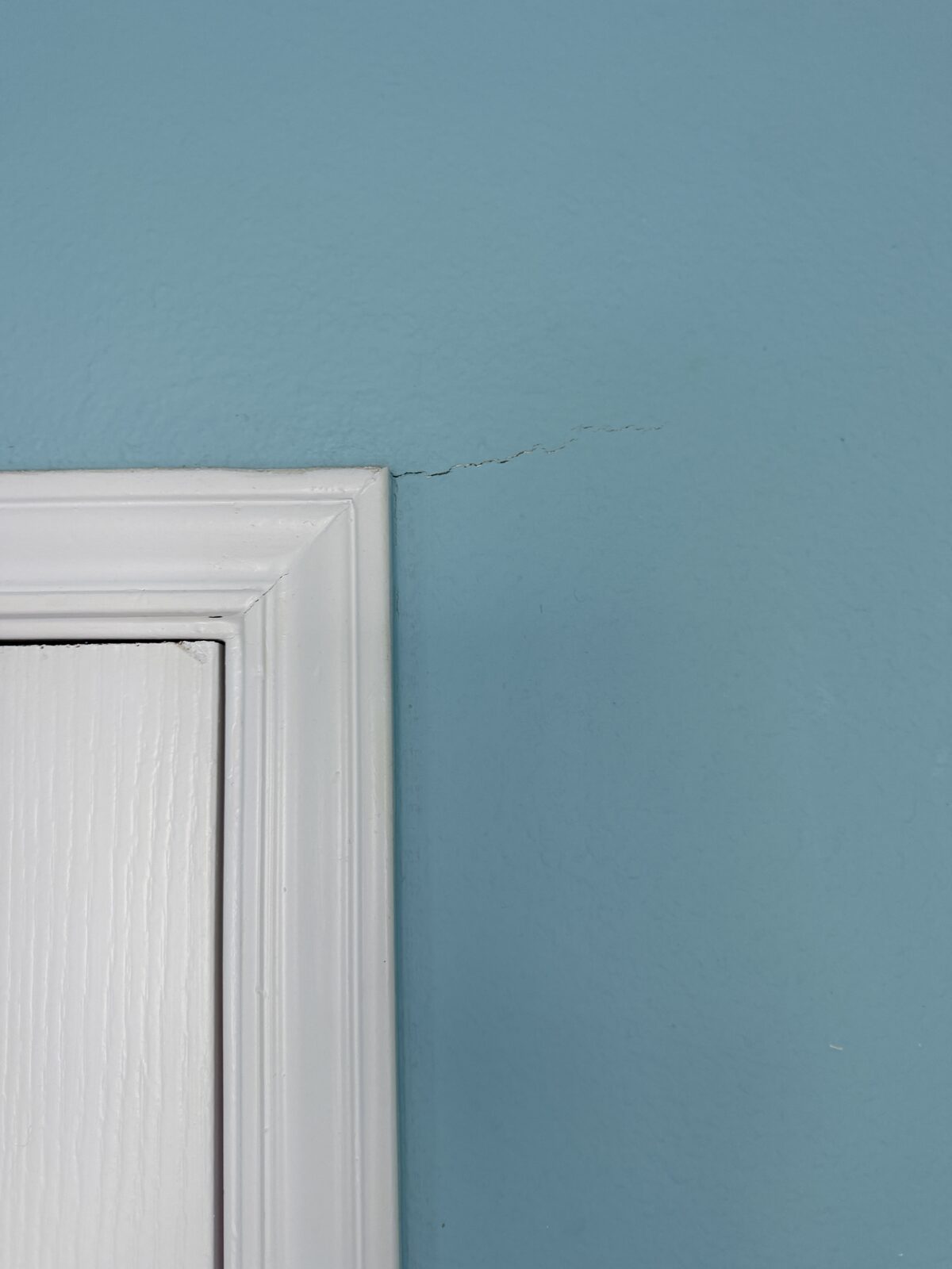 Hairline crack running from a door trim to the ceiling from foundation movement