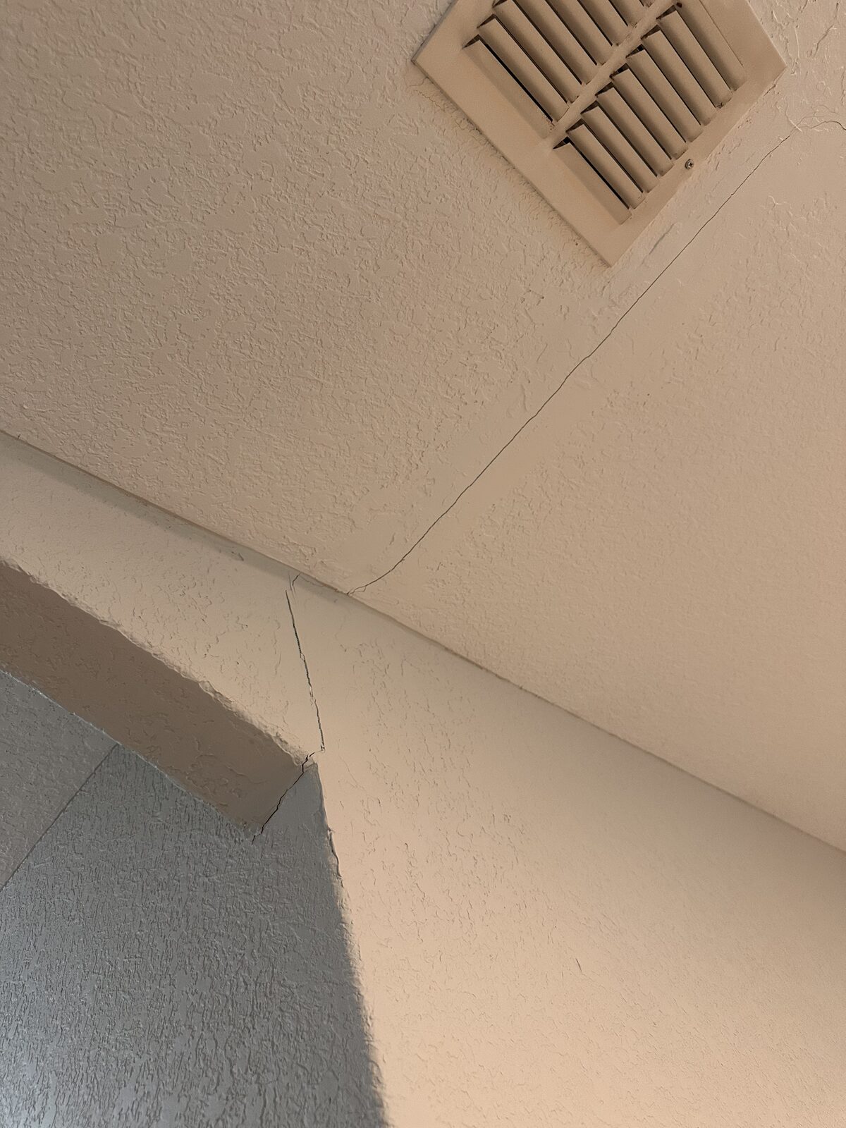 Hairline drywall crack at an interior wall corner near a return-air vent in a settling home