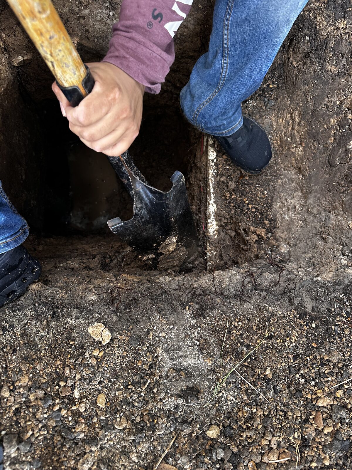 Crew member hand-digging a square pier hole beside a foundation for pier installation