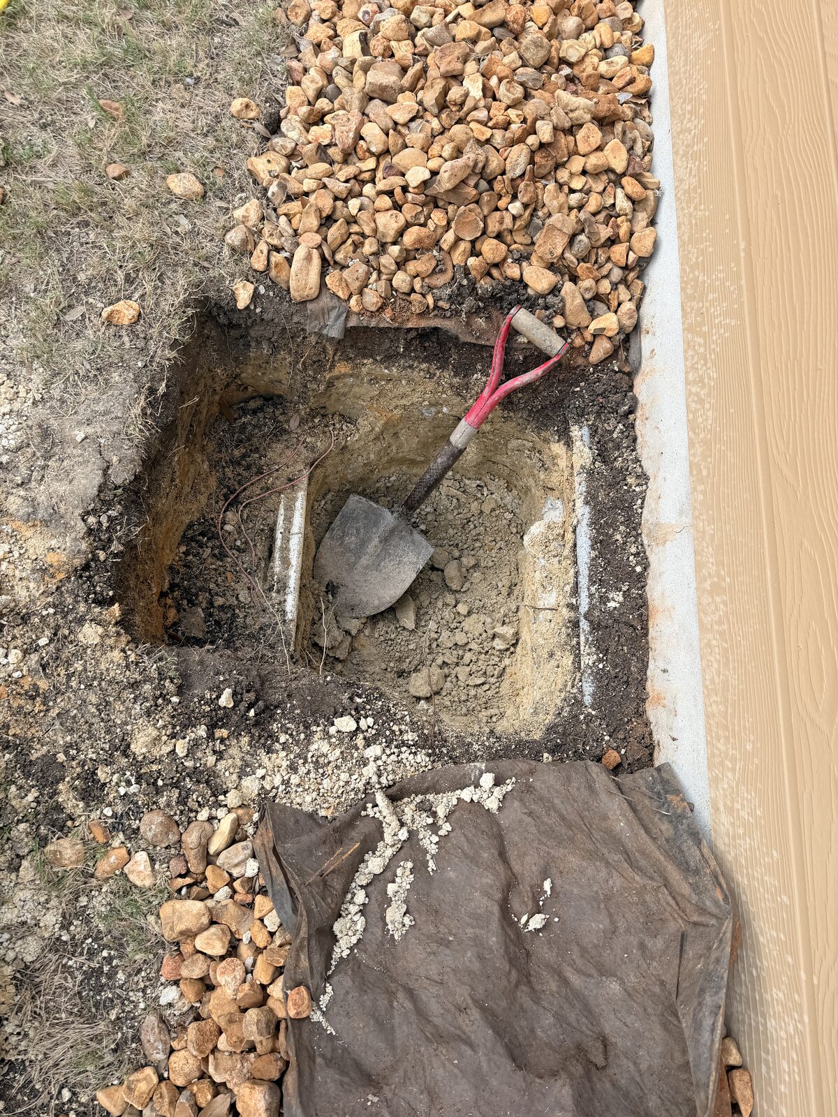 Shovel and pick inside a hand-dug pier hole beside a home's foundation during repair work