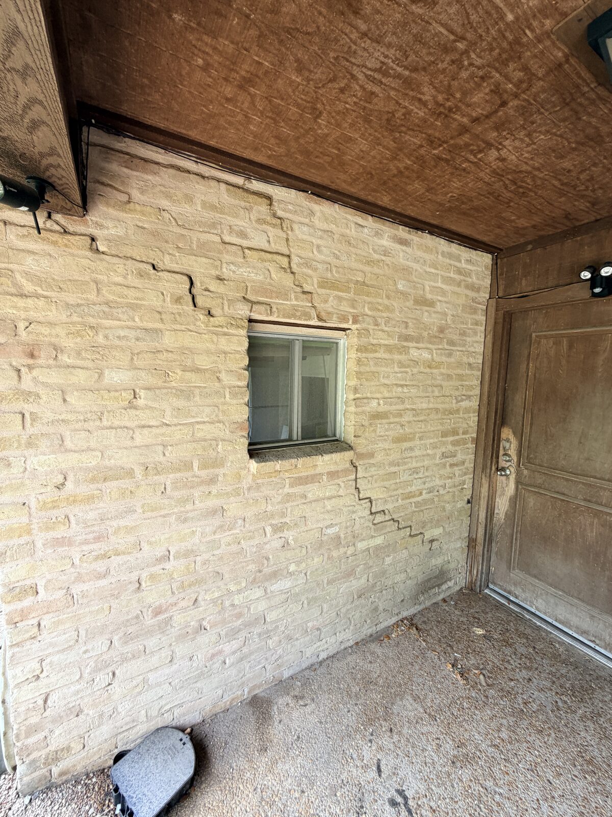Network of cracks in brick around a small window at a porch corner, documented during a foundation inspection