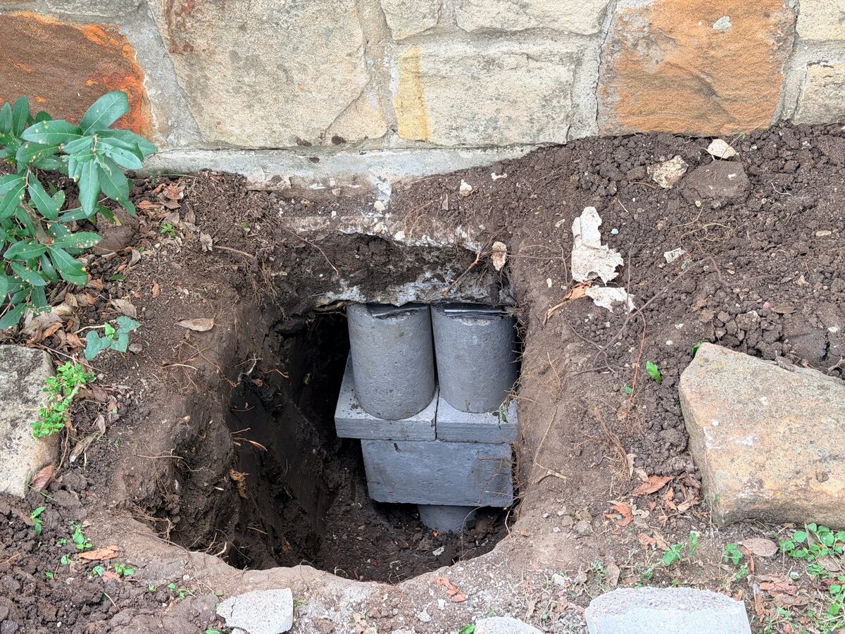 Hybrid pier in a hand-dug hole under a stone veneer wall, concrete sections and a cap block set under the beam