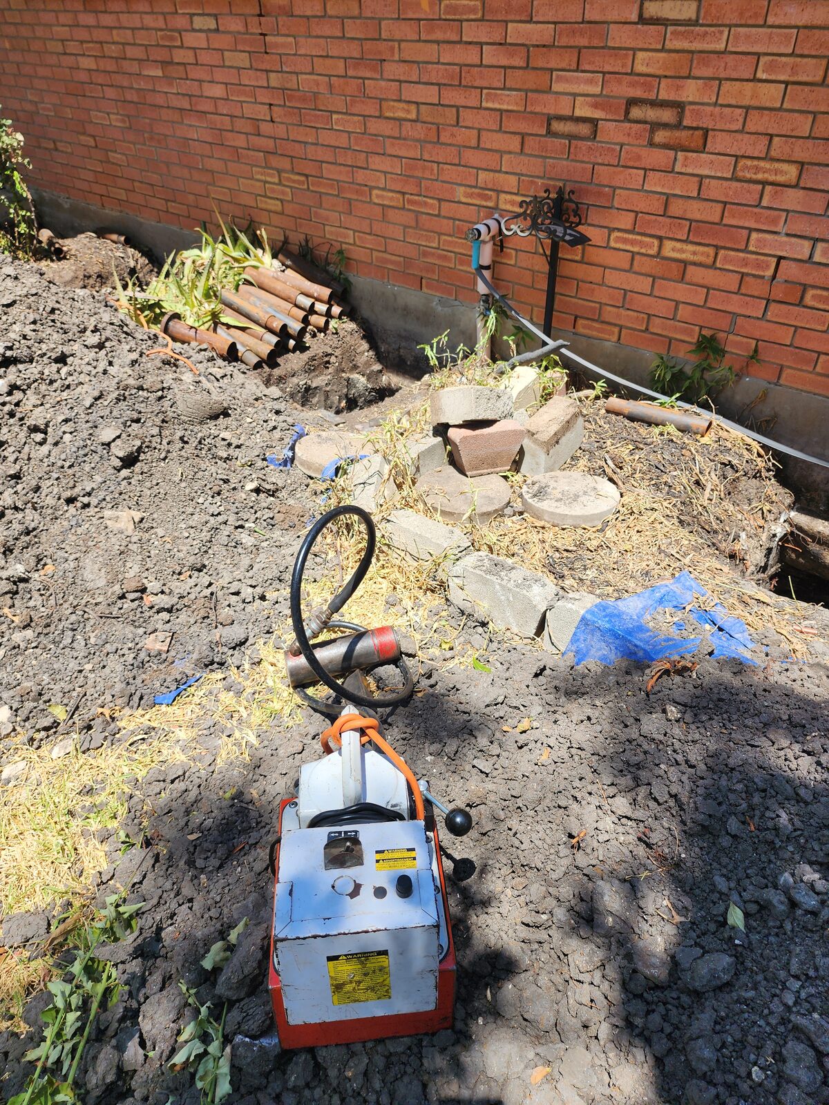 Portable hydraulic pump staged at an excavation, used to drive foundation piers beside a brick home