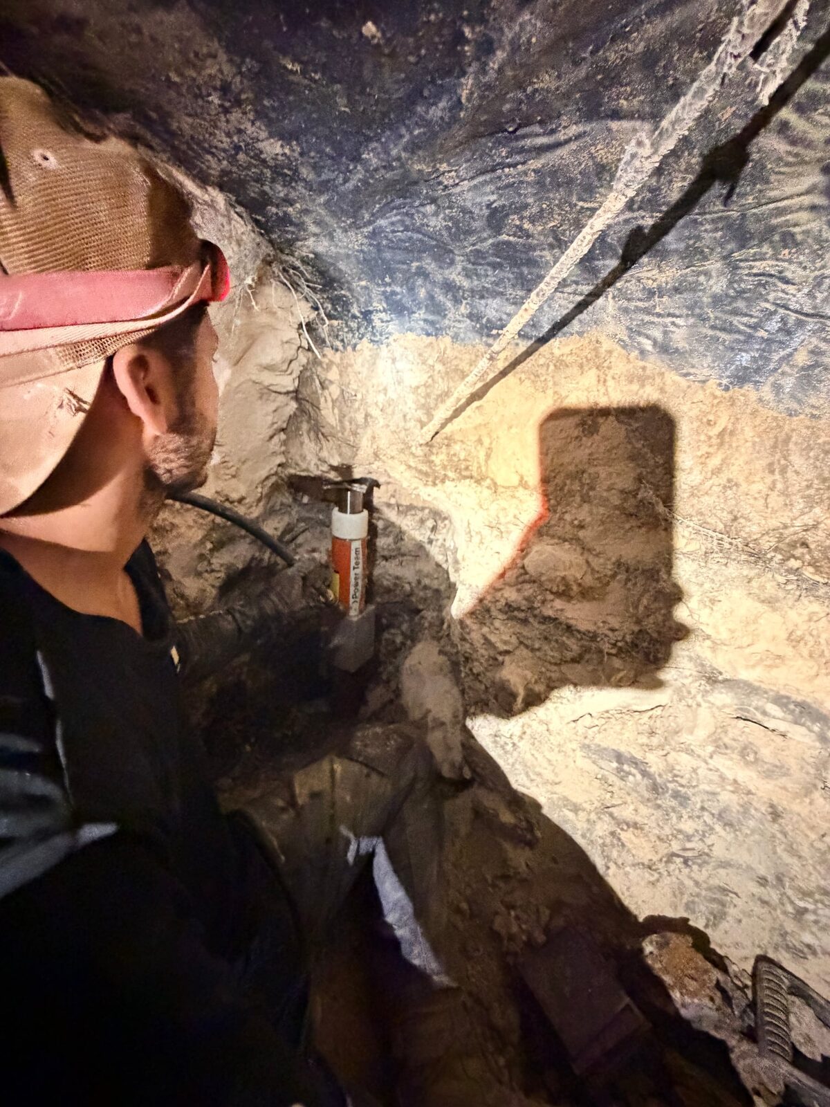 Crew member watching a hydraulic ram drive a pier under a slab foundation inside a tunnel