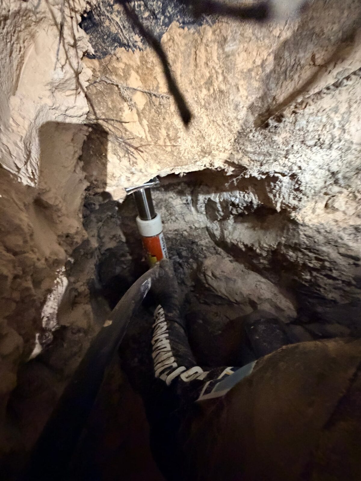 Hydraulic ram braced against the bottom of a slab foundation inside a tunnel, hose running to the pump