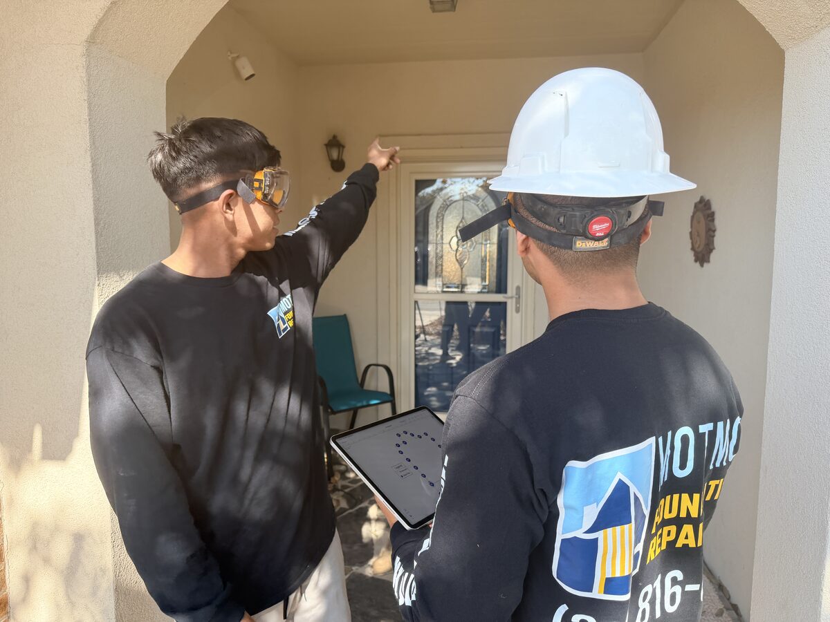 Inspection team checking a front porch door frame for foundation movement with a tablet elevation map