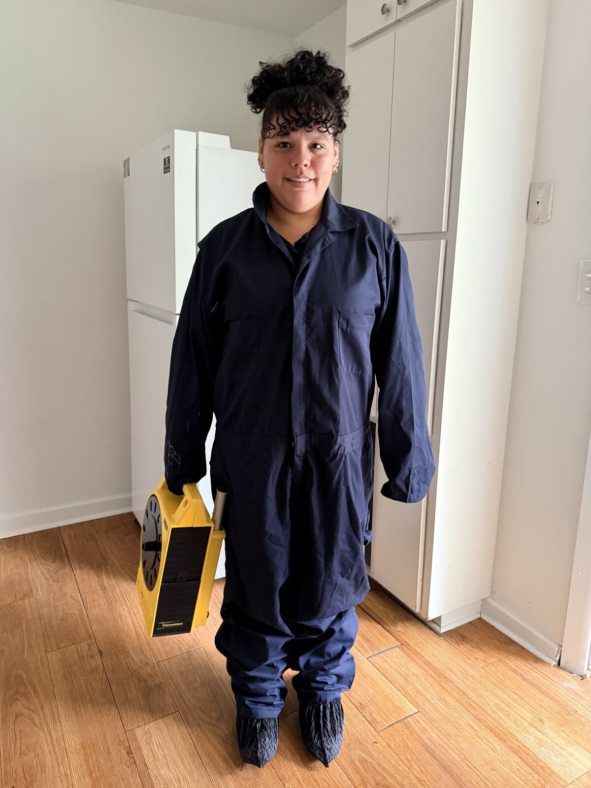 Inspector in navy coveralls holding a yellow elevation measuring level in a kitchen