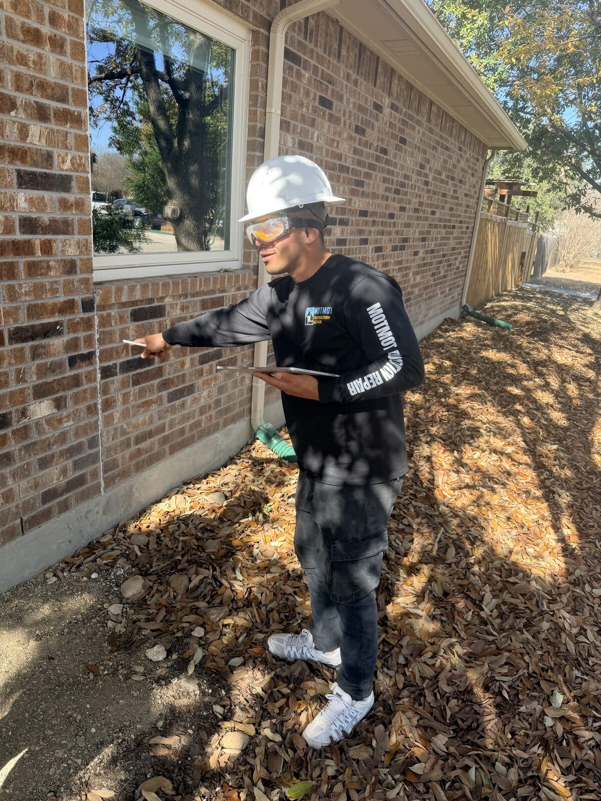 Inspector pointing to a crack in brick veneer near a window, a common sign of foundation settlement