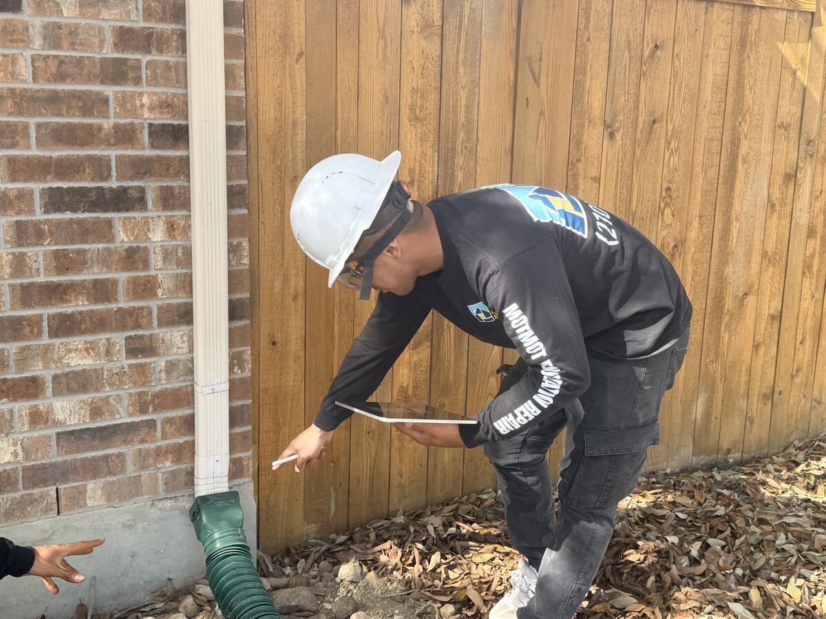 Inspector pointing out a downspout extension at the slab corner that carries water away from the foundation