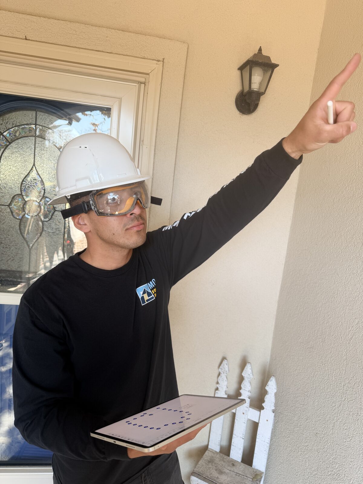 Foundation inspector pointing out stucco damage above a porch while logging notes on a tablet