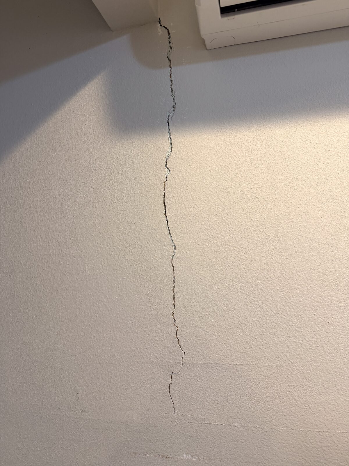 Closeup of a jagged drywall crack caused by foundation movement beneath an interior beam