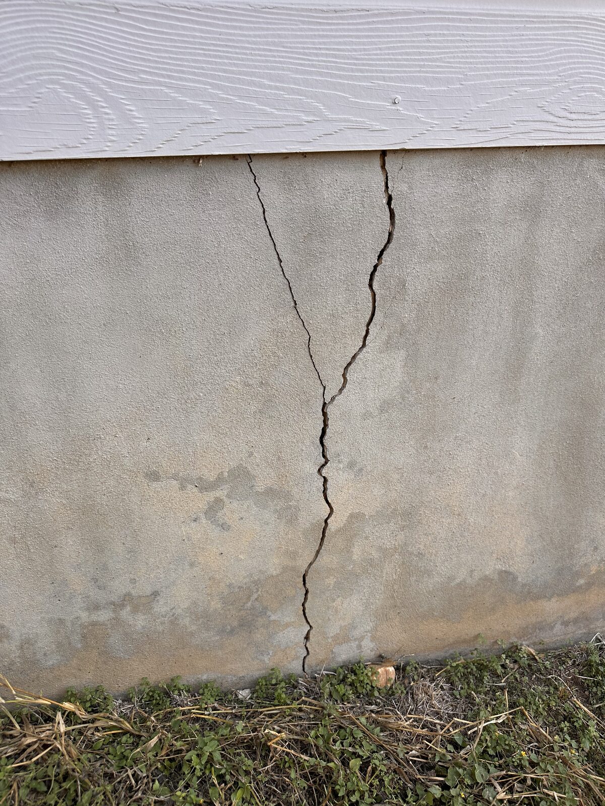 Jagged vertical crack running the full height of a concrete stem wall beneath lap siding