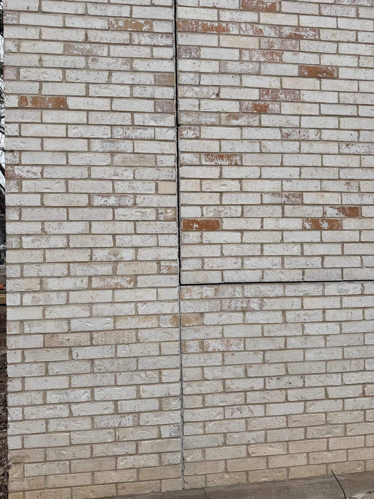 Opened vertical joint in a white brick wall with a horizontal crack branching off and courses misaligned across the seam