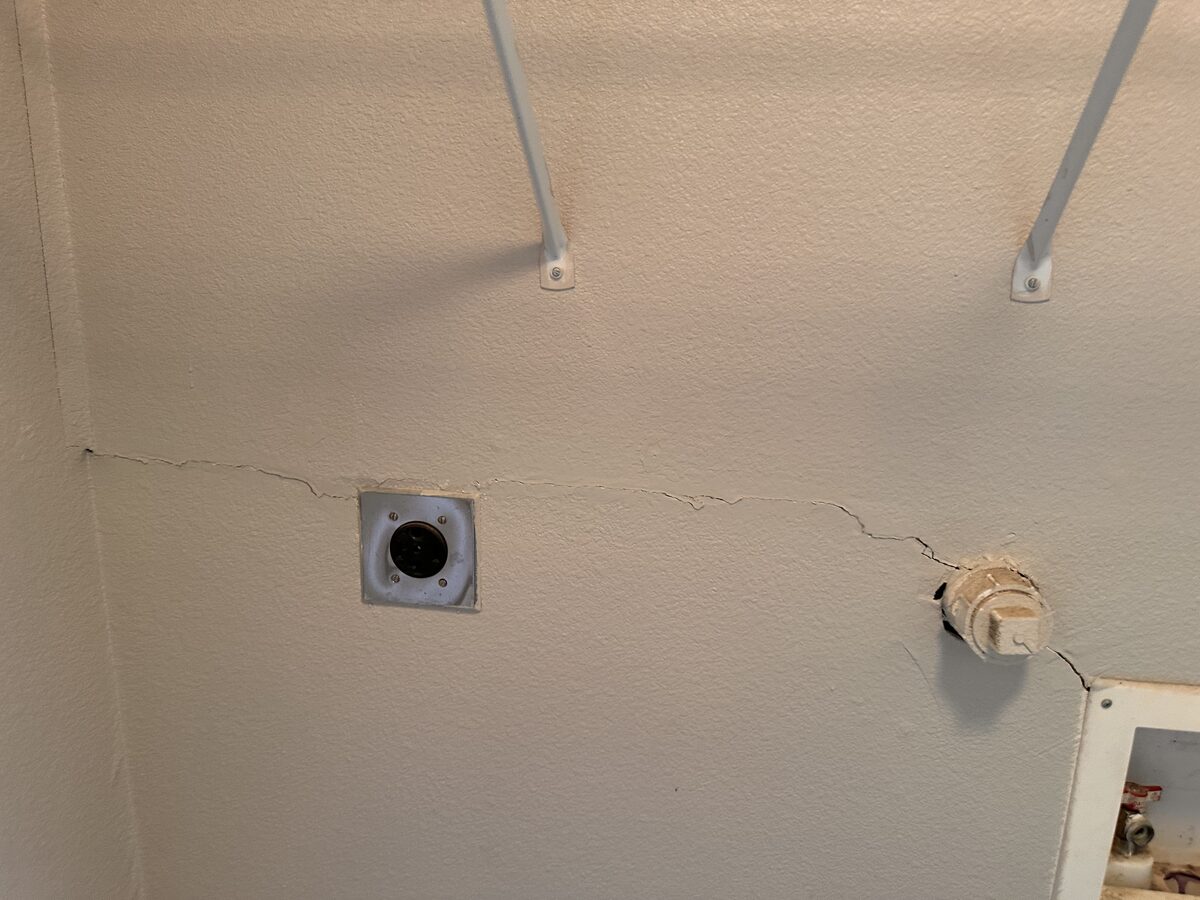 Long drywall crack running across a laundry room wall near the dryer vent, a sign of foundation movement