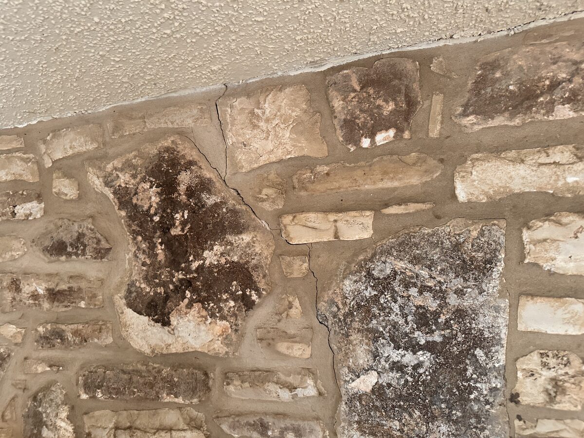 Crack tracing the mortar joints where a stone masonry wall meets the ceiling line