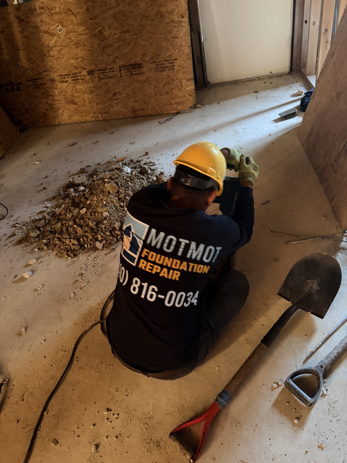 Motmot Foundation Repair crew member in a hard hat breaking out a garage slab for an interior pier