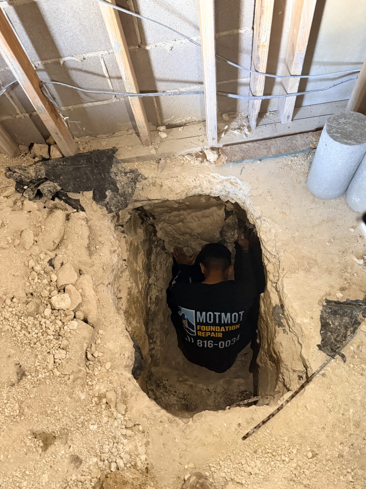 Motmot Foundation Repair technician working inside a hand-dug pier pit beneath a home's foundation