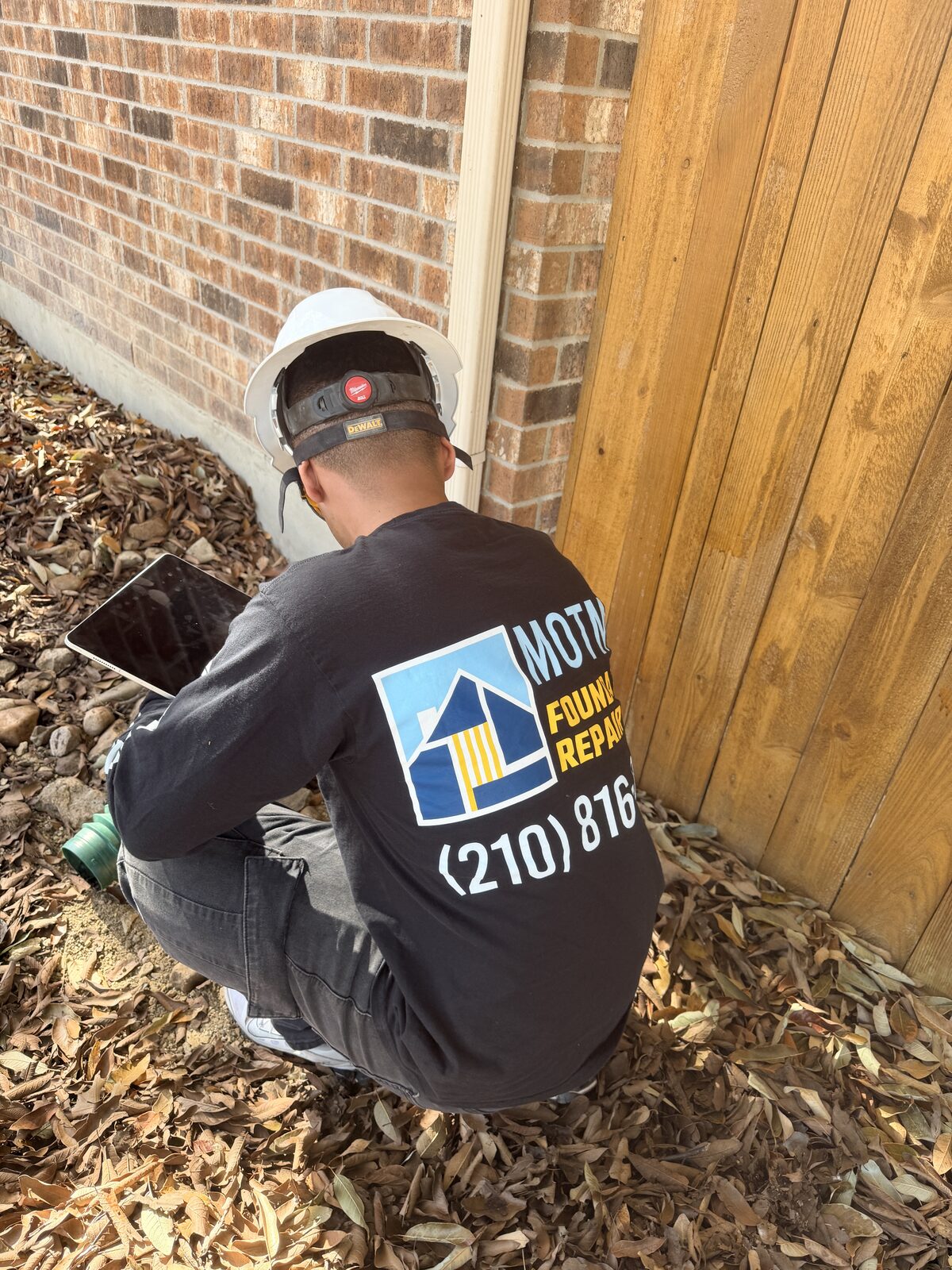 Motmot Foundation Repair technician logging drainage notes on a tablet at a home's foundation corner
